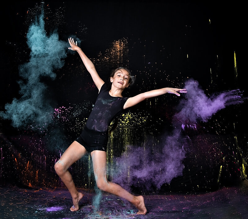 Dancer dressed in black tossing blue and purple colored chalk against a black backdrop in Morris County 