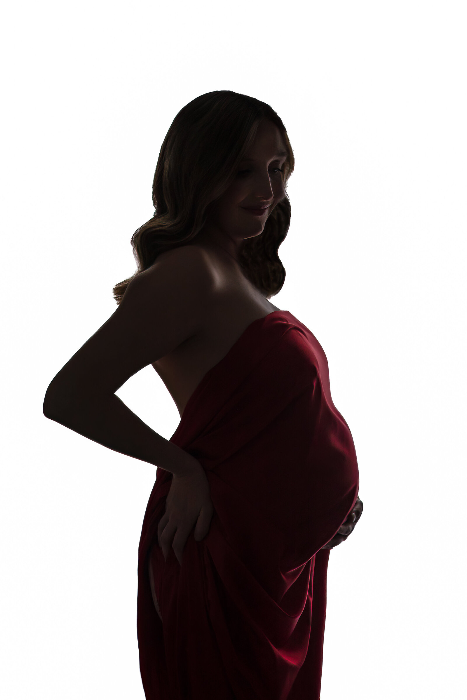 A pregnant woman wrapped in red fabric with her hands on her stomach and back for her maternity pictures in Huntsville Alabama