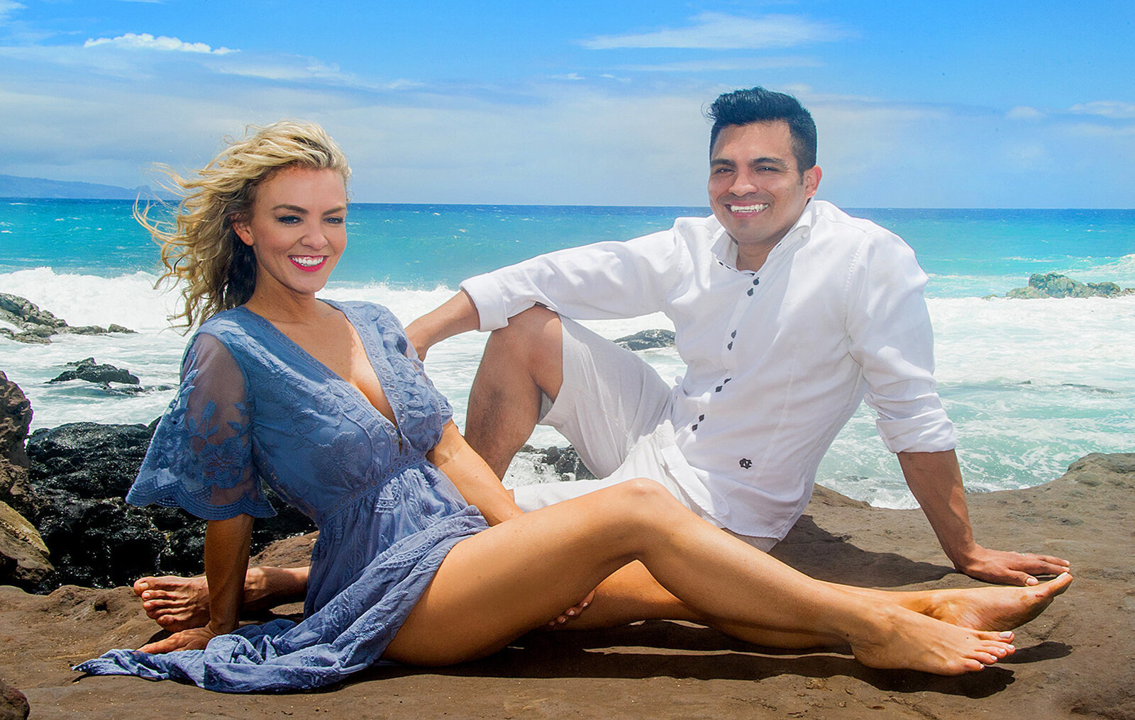 Engagement couple sitting on the rocks in Oahu  beach on a sunny day, wearing a nice blue and white clothes.