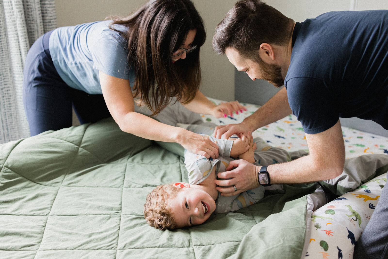 Mom and dad tickle laughing pre-schooler as he tries to escape