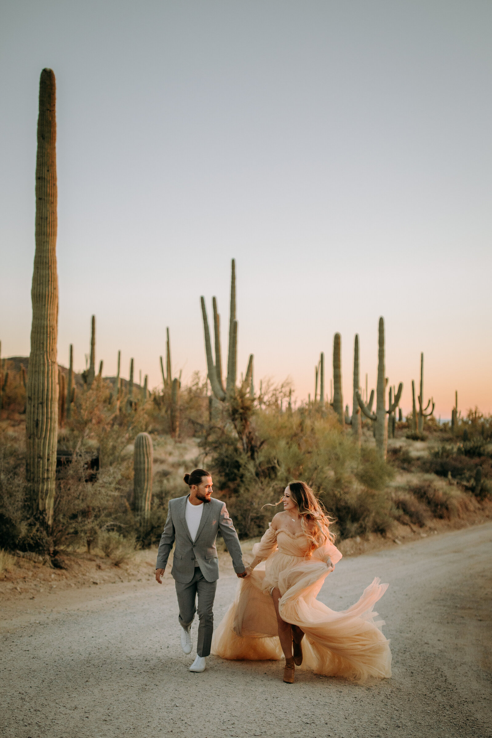 Couple running towards camera in suit and dress with cactus in the desert