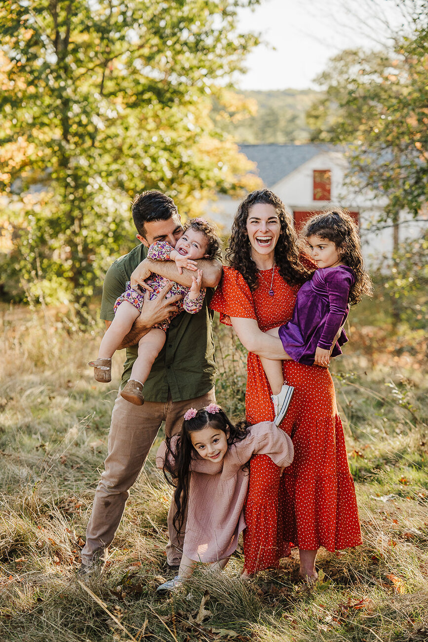 family of five posing with three girls laughs at the camera