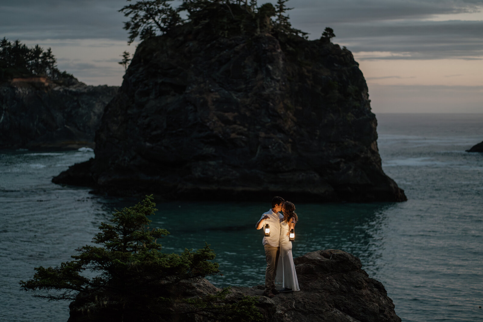 Couple kissing at Secret Beach during Blue hour holding lanterns during their Adventure Elopement along the Oregon Coast.