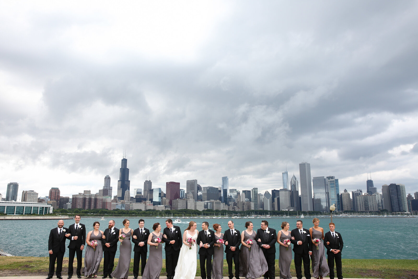Bride and groom pose for portrait with their wedding party on the water with Chicago skyline in the background