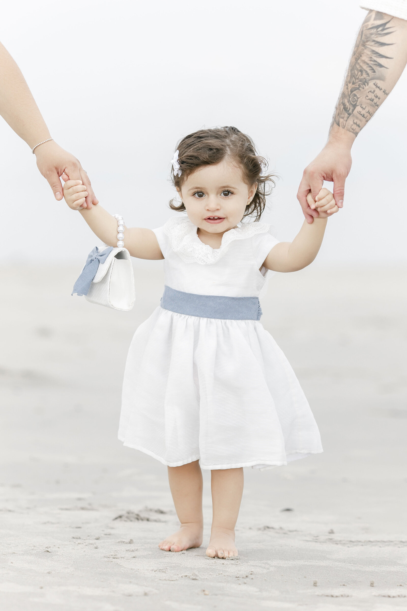 little girl holding parents hands standing on ocean city beach photographed by new jersey family photographer