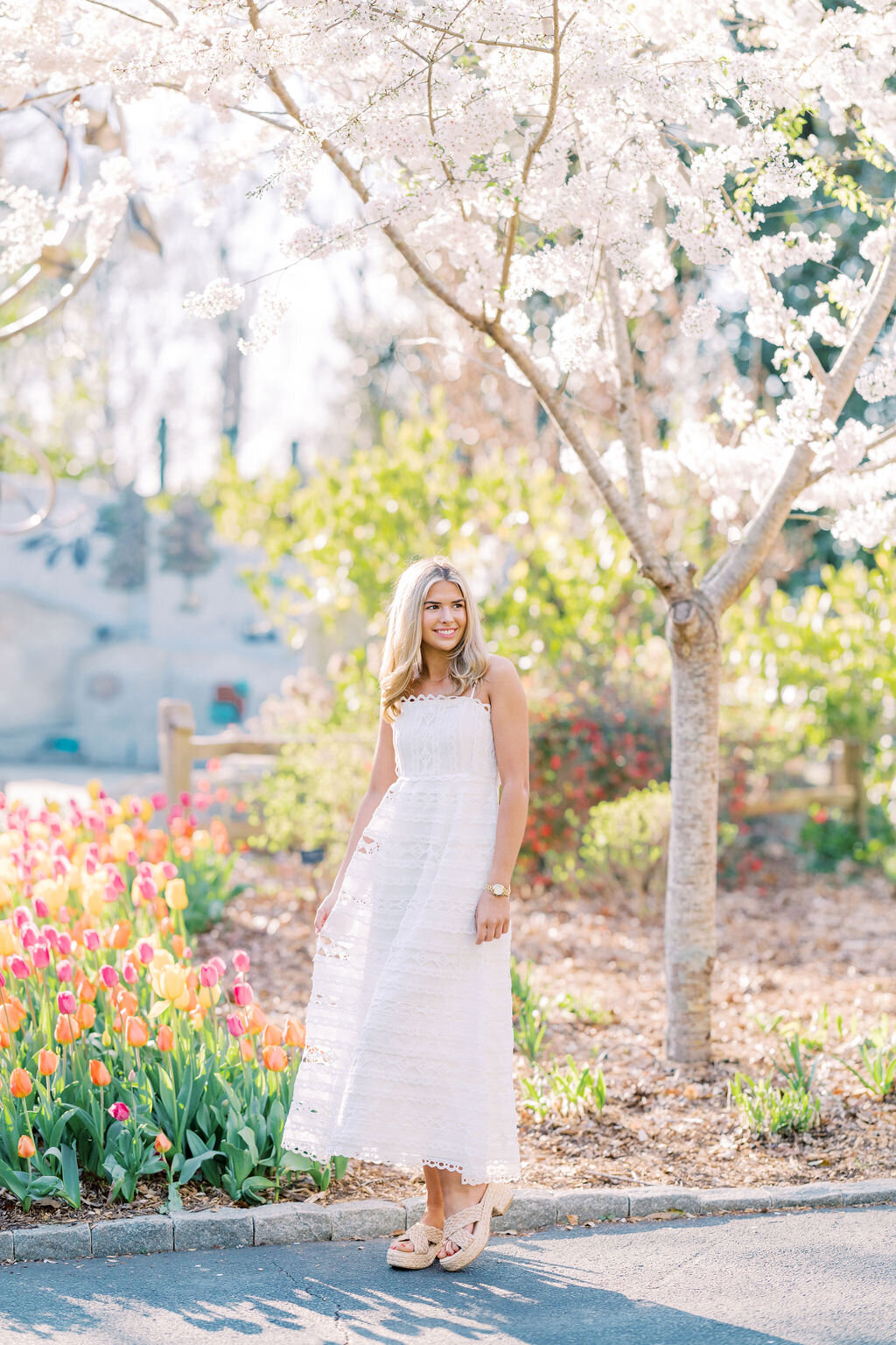 Girl in white dress smiles under tree in Athens Botanical garden in Springtime