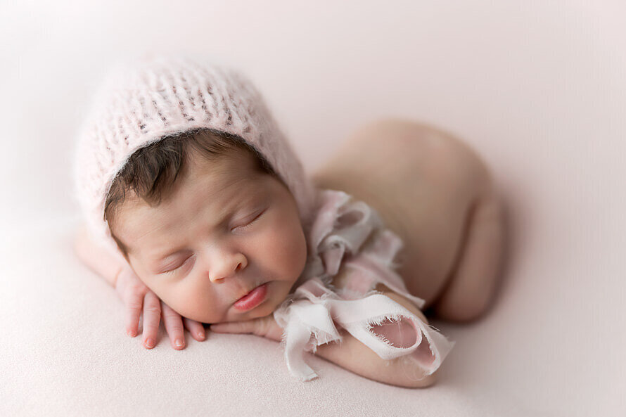 Newborn baby with pink bonnet on pink backdrop.
