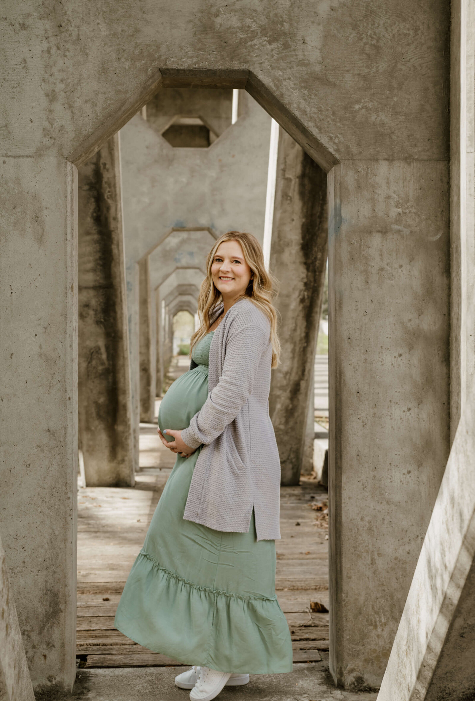 Pregnant woman in sage dress posing under bridge.