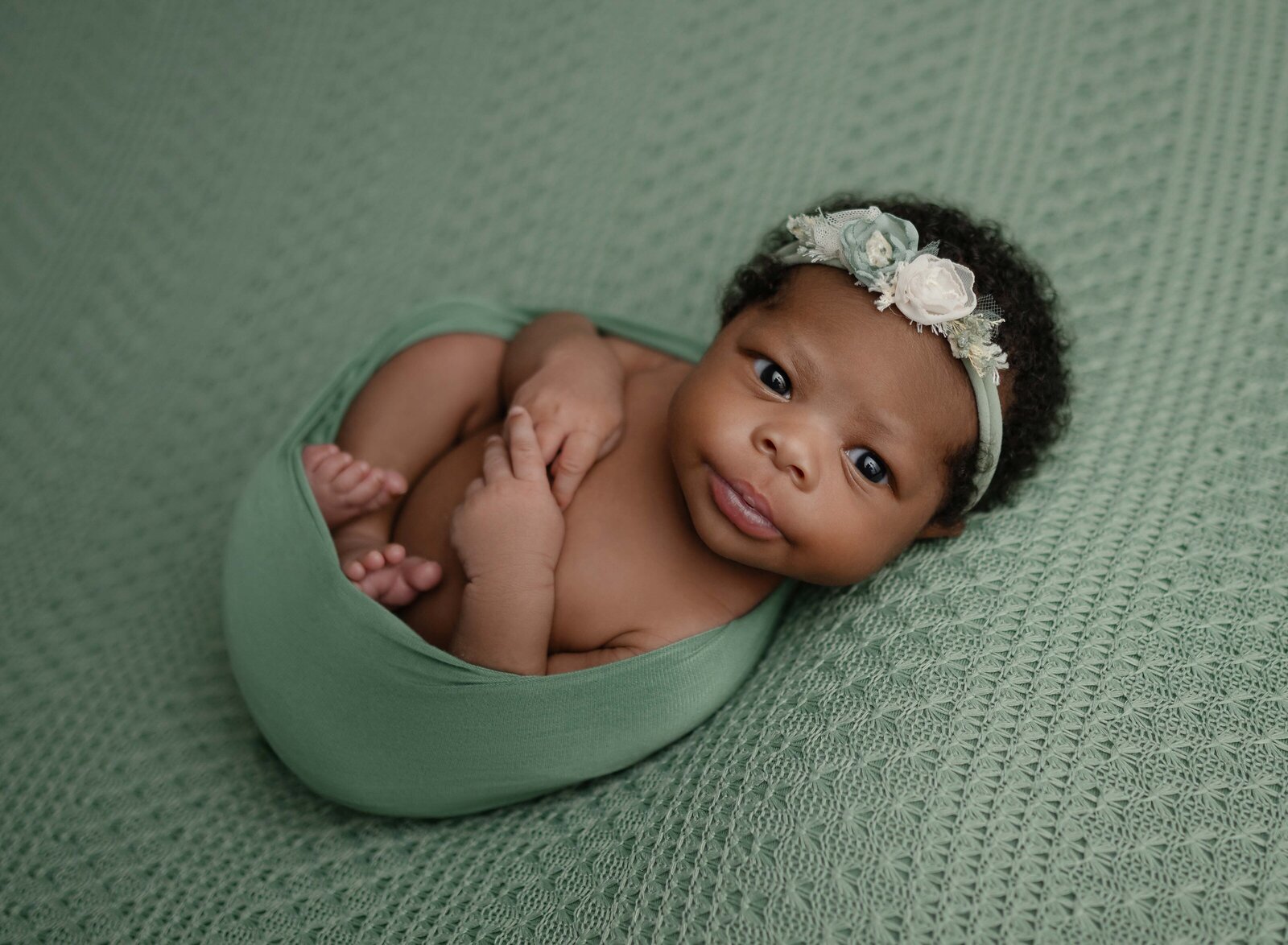 Baby girl in greed swaddle with eyes open and looking at camera. Photographed in Atlanta baby photo studio.