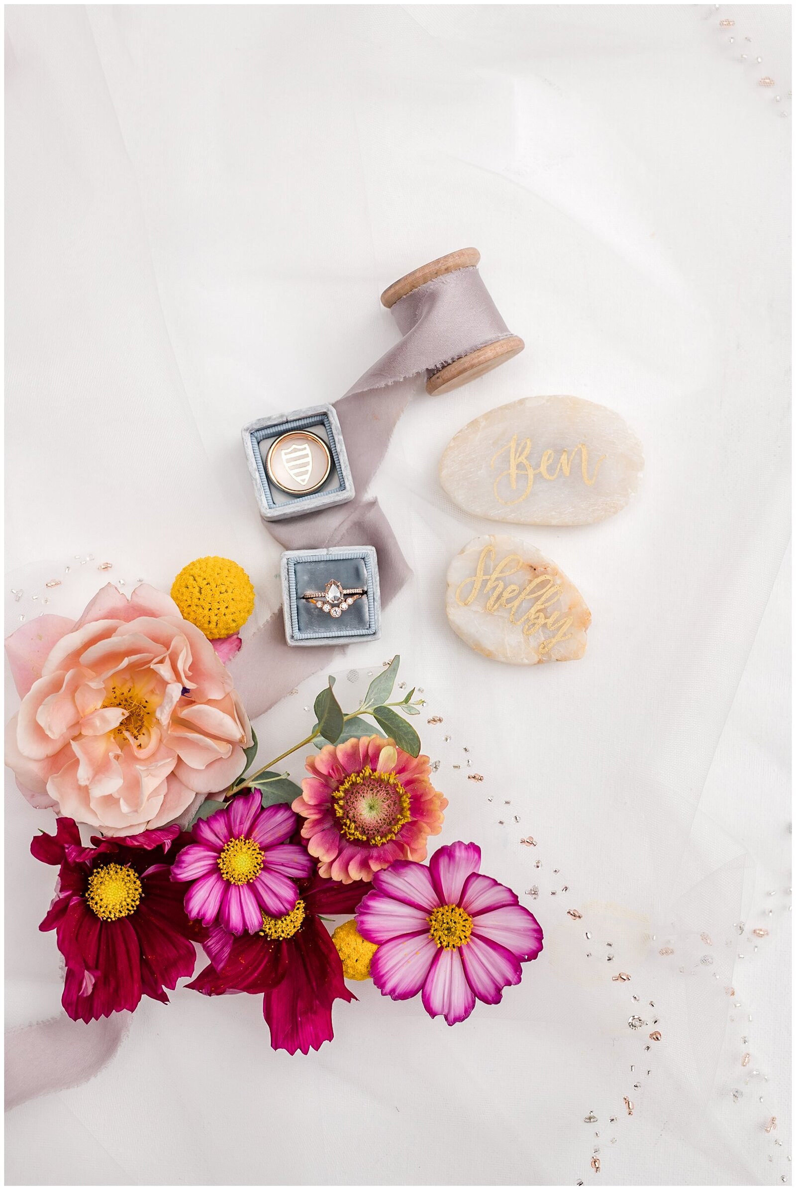 Flatlay of wedding rings in blue box next to flowers and stones