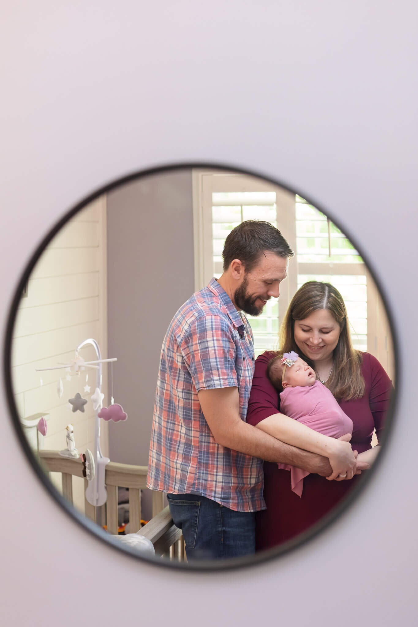 A mirror with the reflection of a mom and dad holding their newborn daughter.
