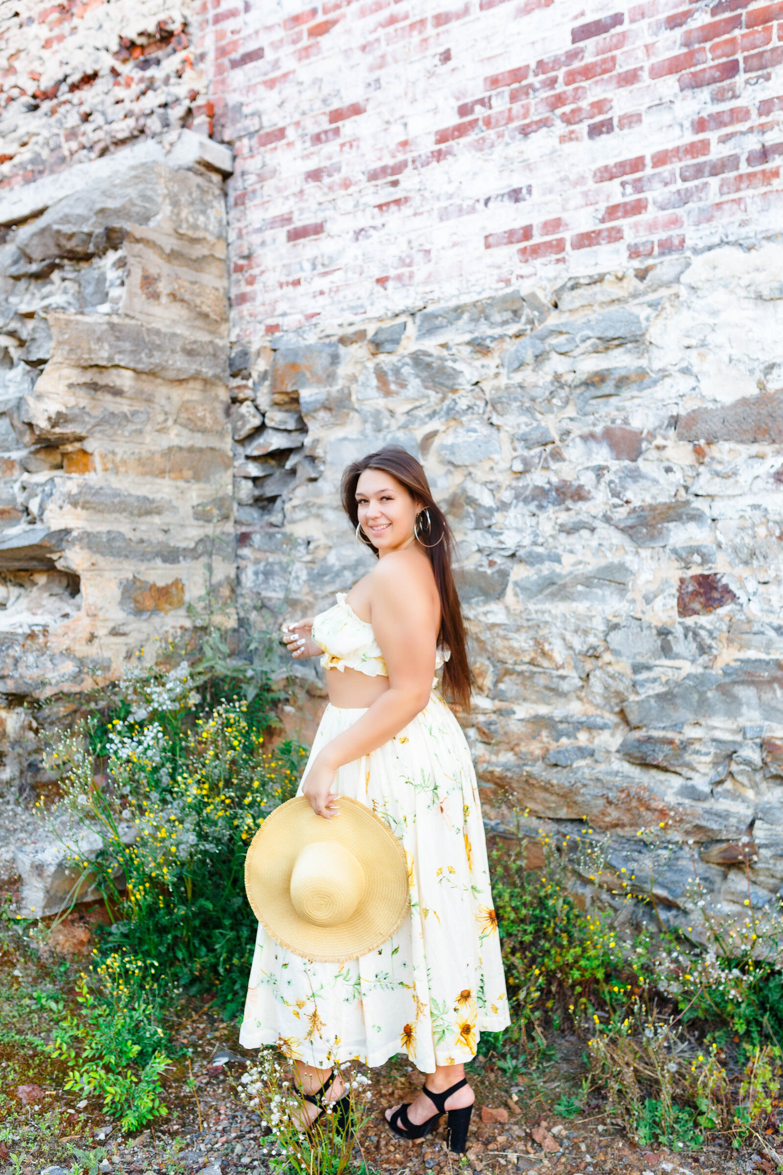senior dressed in boho dress with hat in front of rock wall
