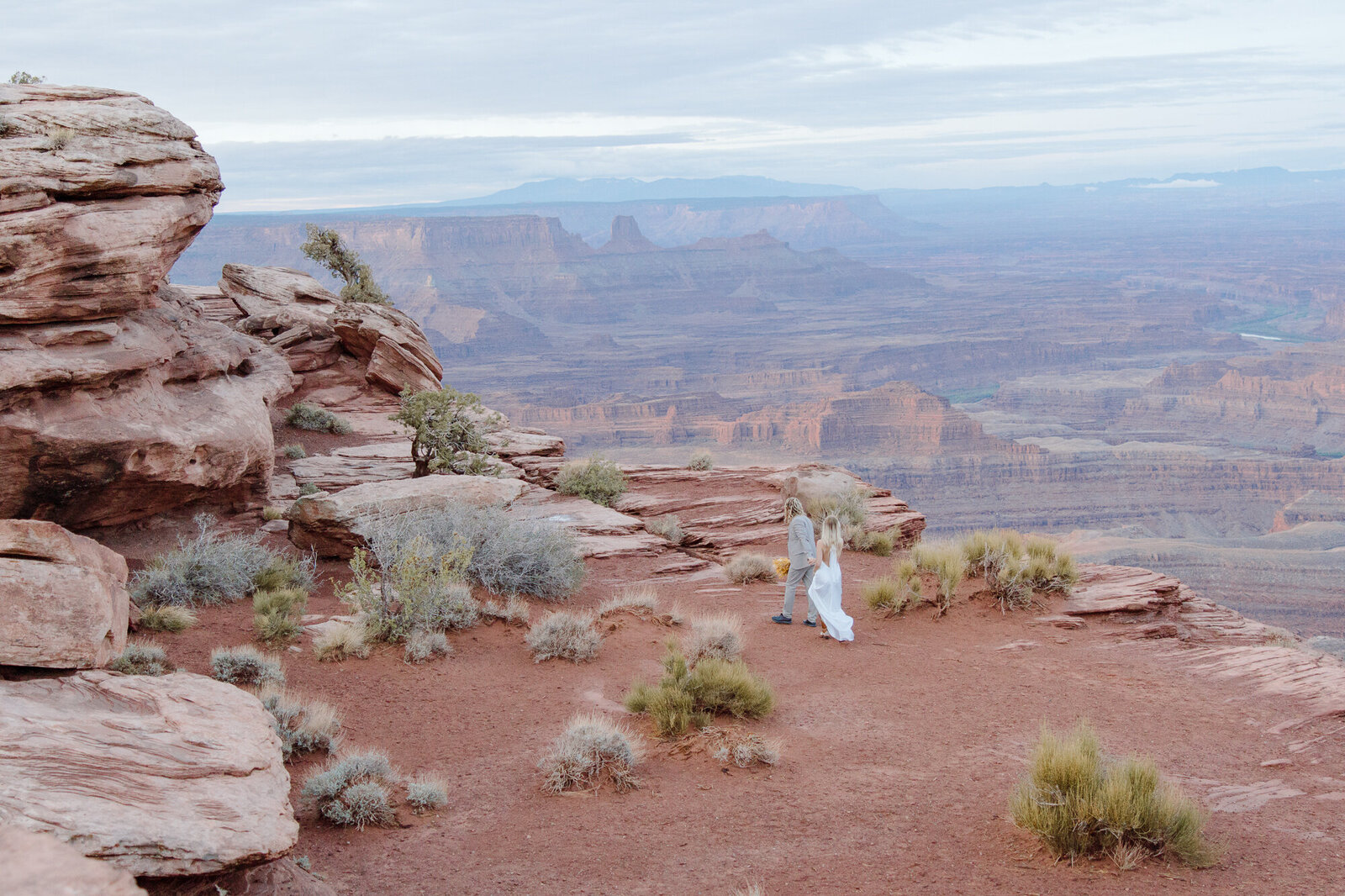 groom leading bride to ceremony on the red rocks during sunrise 