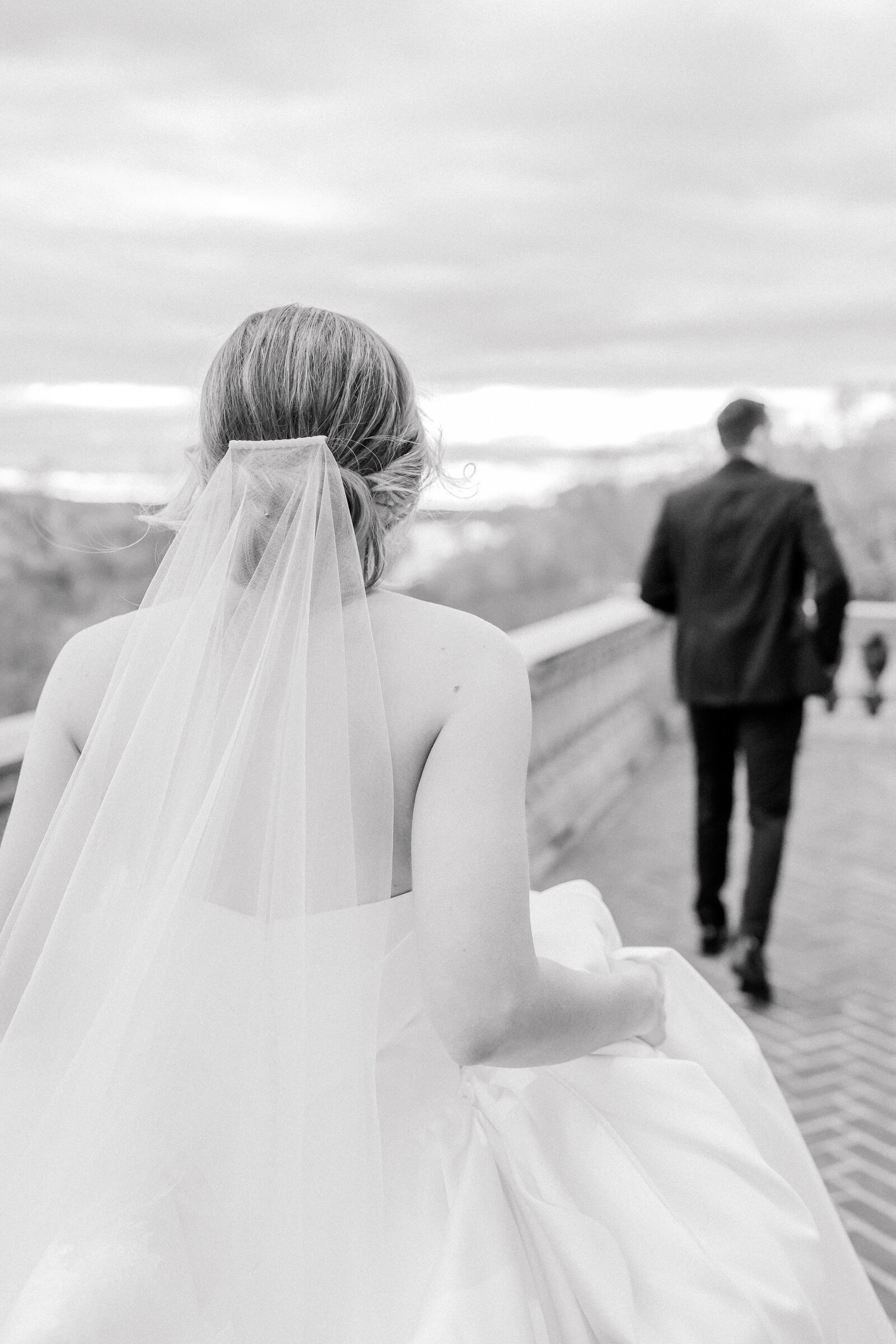 Candid, black and white, of the bride following the groom down a brick walkway