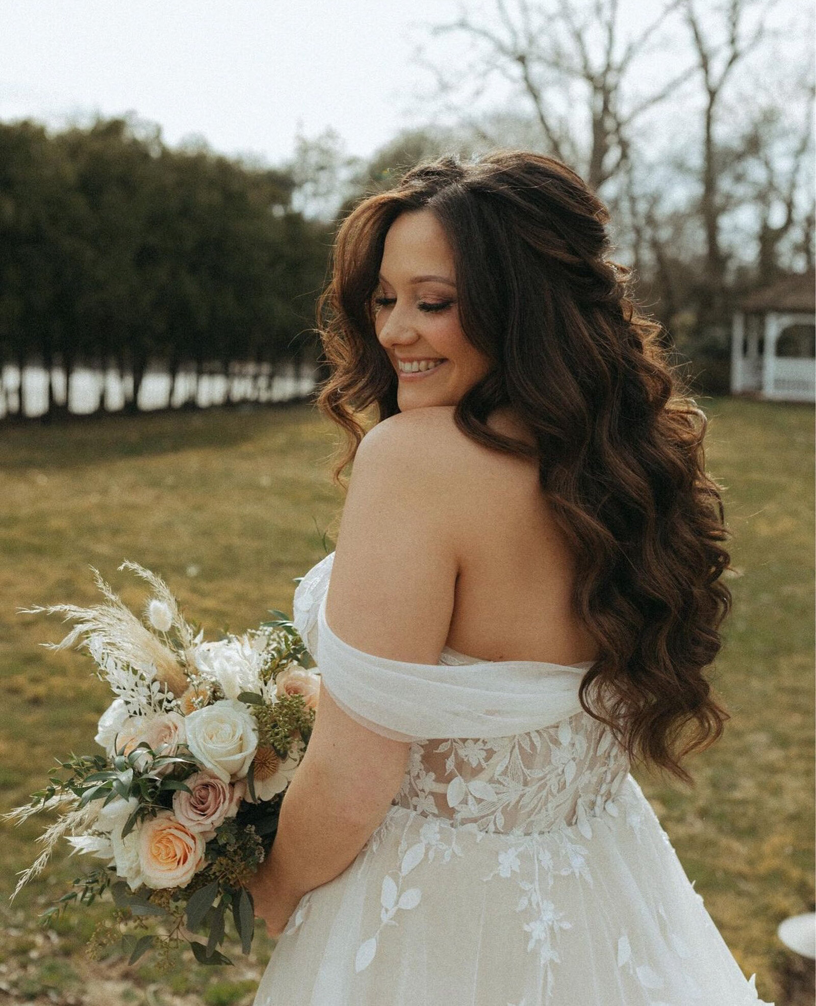 bride with long, wavy hair smiles joyfully while holding a bouquet of flowers