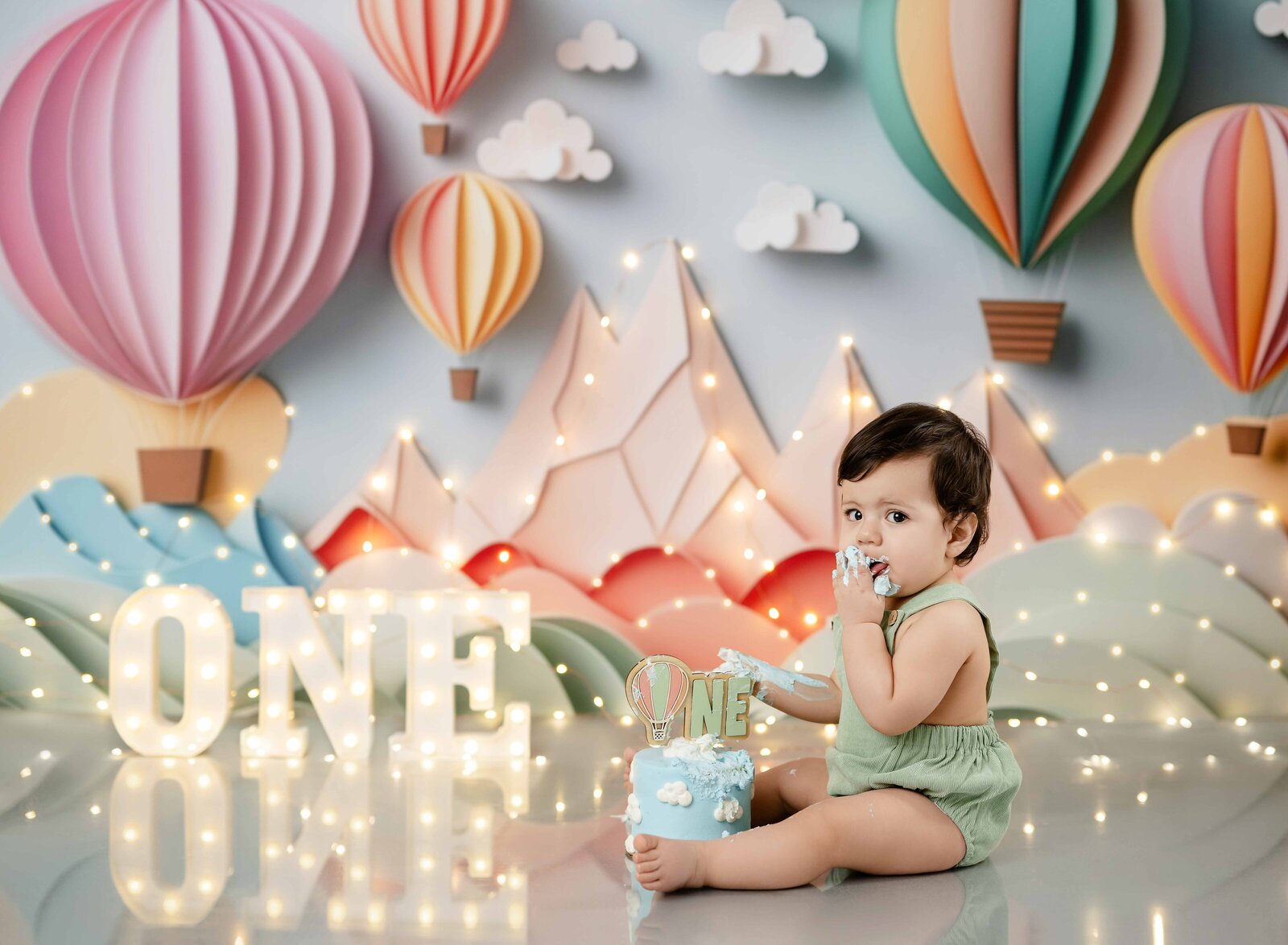 Baby sitting in front of a travel themed cake smash and eating a birthday cake.