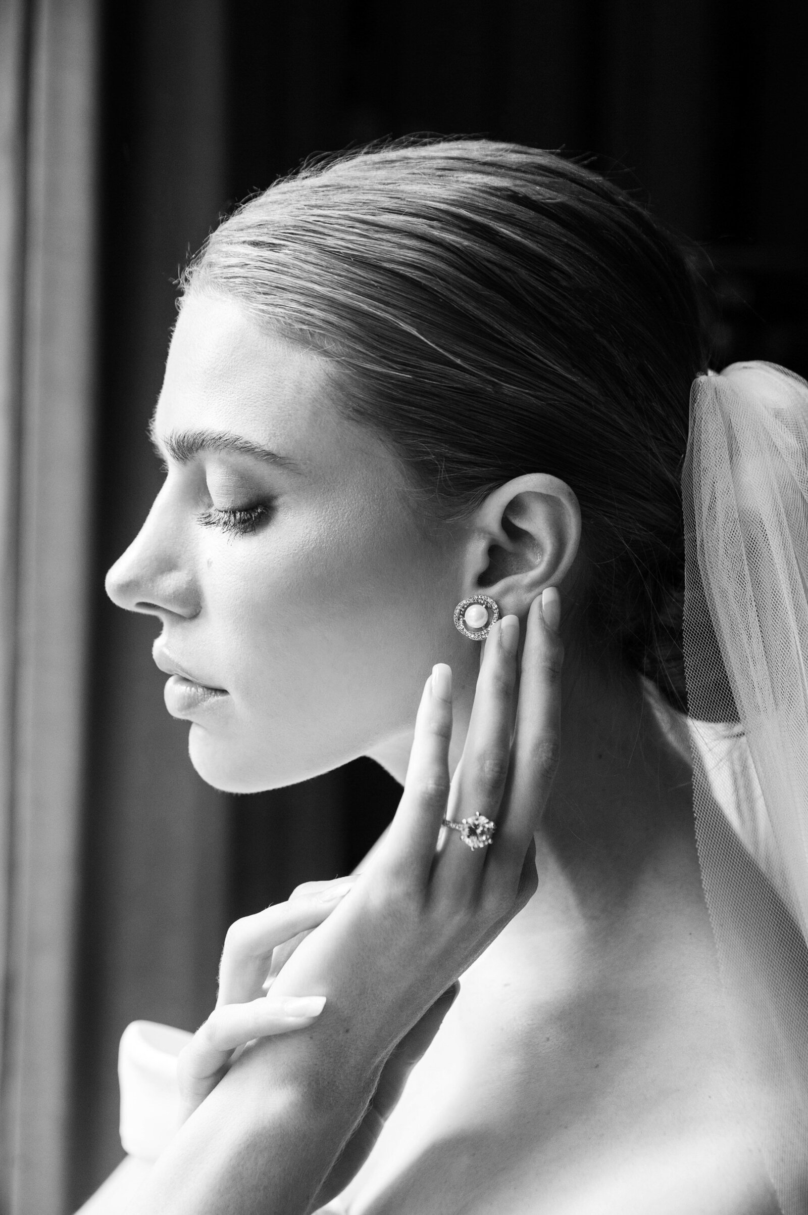 black and white portraits of bride putting in her pearl earrings