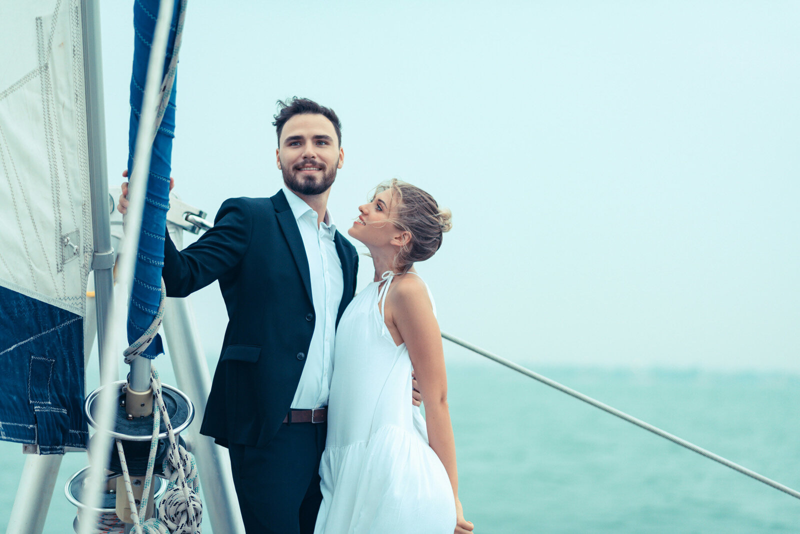 man holds onto the boat's rigging while the woman leans against him, smiling and looking up at him