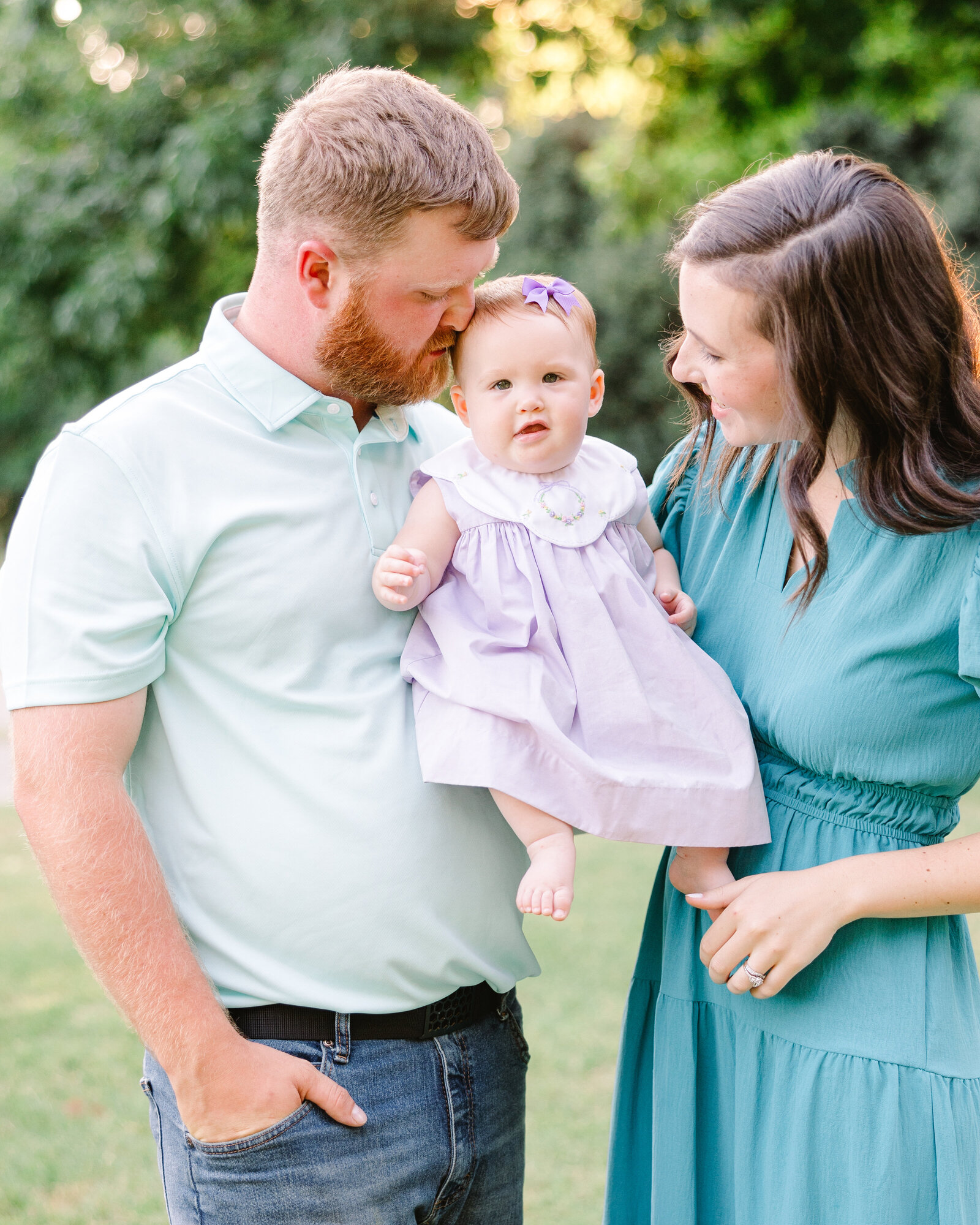 Father kissing baby’s head while mom smiles, showcasing a tender family moment by Abby Bell Photography, Fine Art Portrait Photographer based in Alabama.