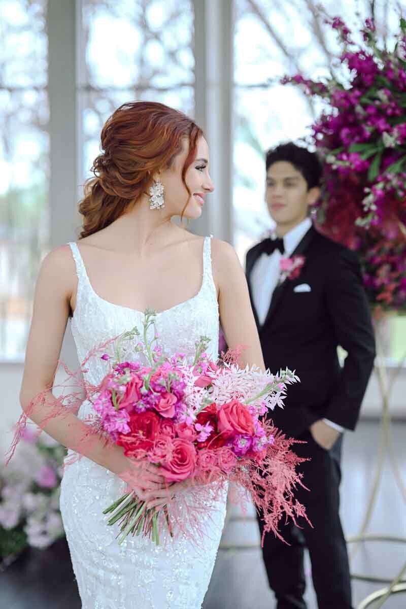 photo of bride holding pink bouquet with groom standing in the background
