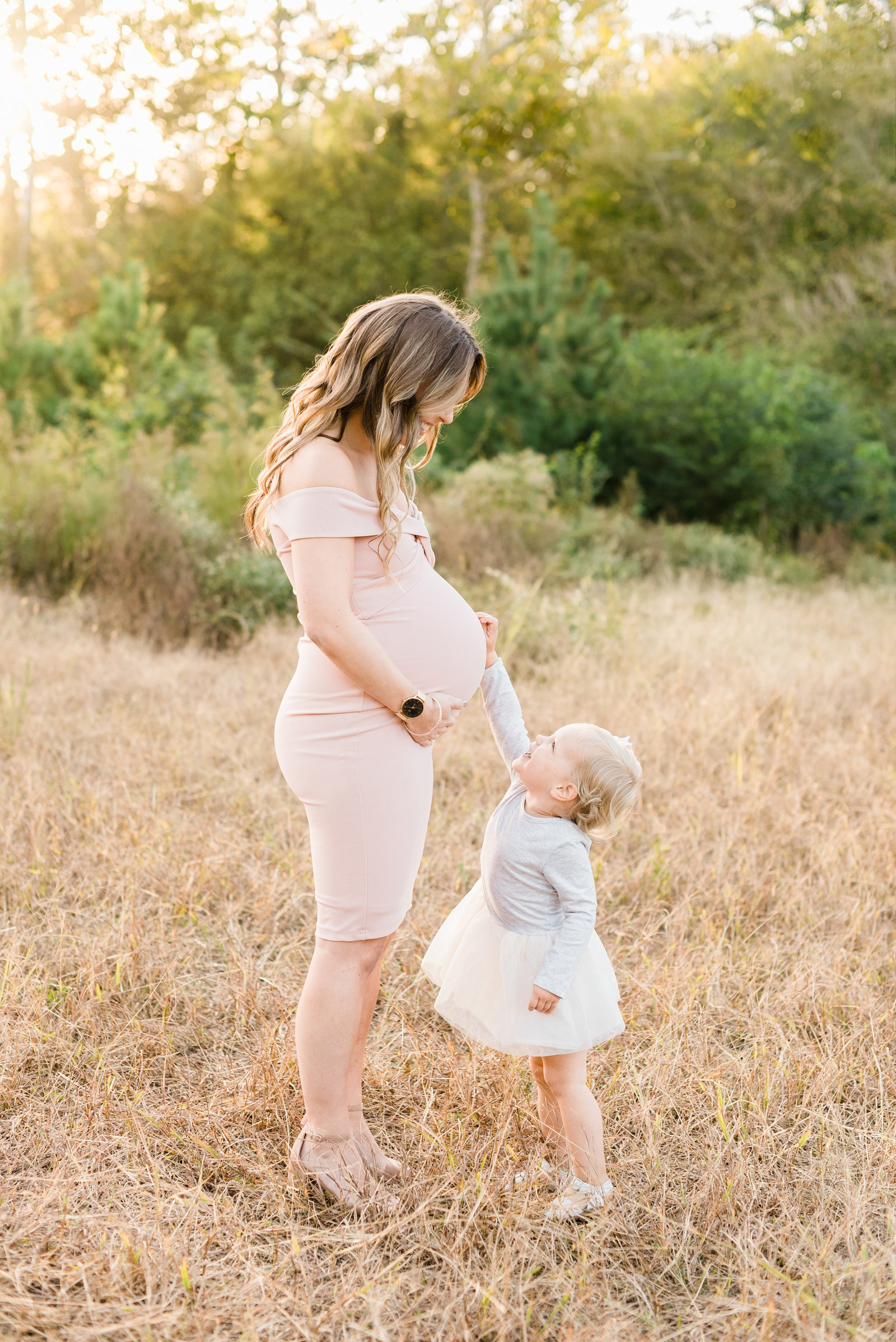 Toddler daughter touching the belly of her pregnant mom and smiling during their Raleigh maternity session. Photographed by Raleigh maternity photographer A.J. Dunlap Photography