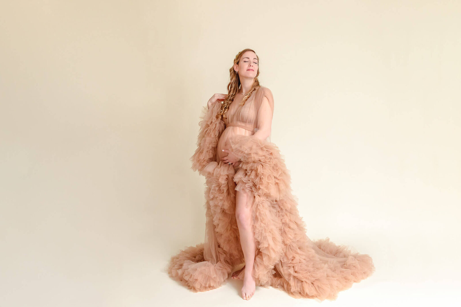 A pregnant woman in a tan robe posing in a Northern Virginia maternity photography studio.