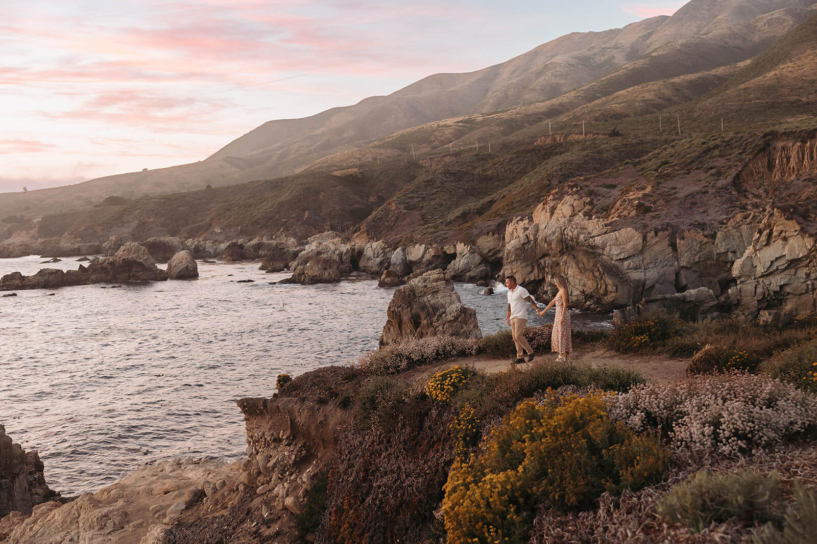 Couple on the Big Sur cliffs under a pink sunset sky