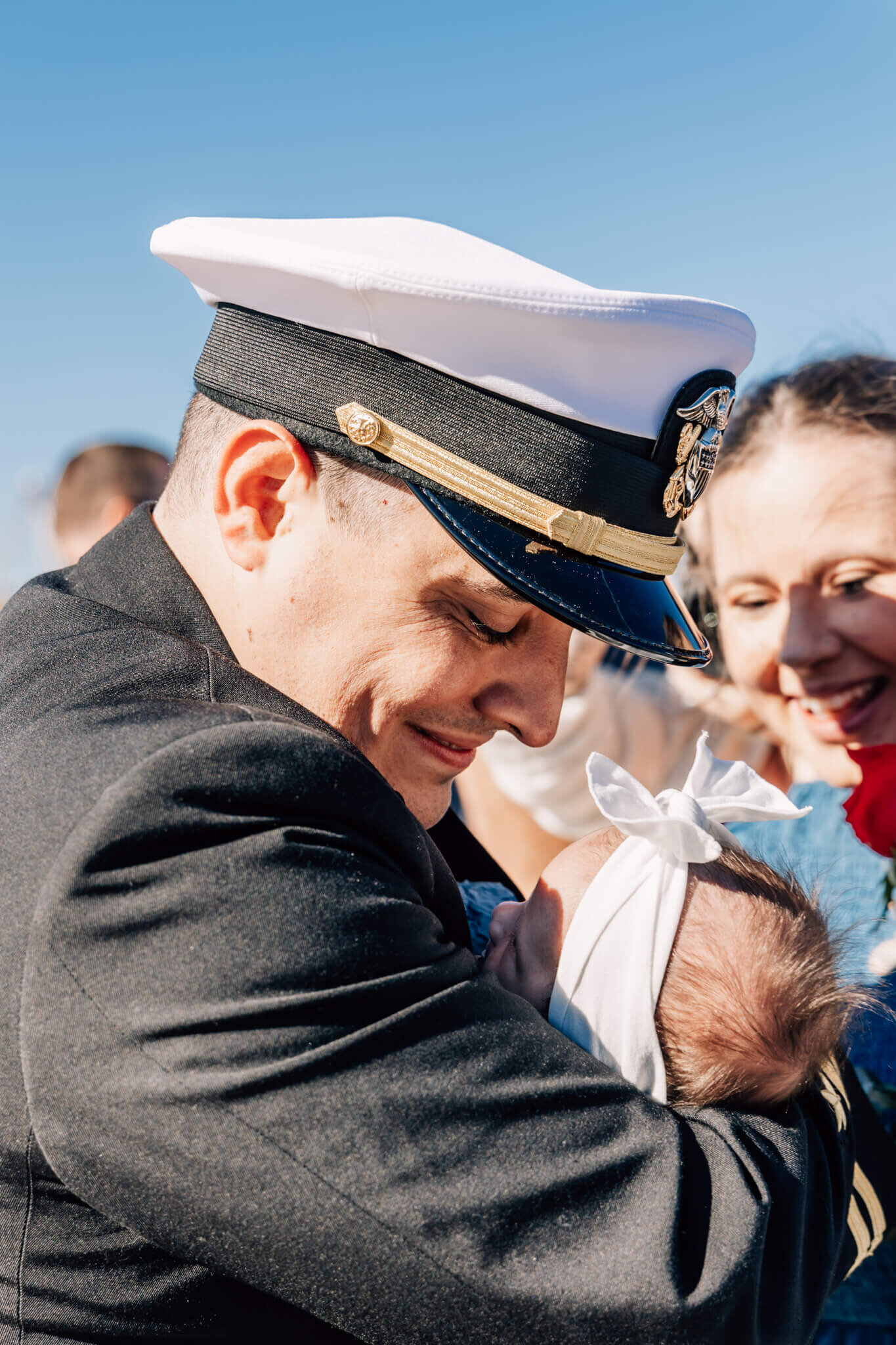 Naval officer looks down at new baby, meeting baby for the first time, at emotional USS North Dakota homecoming in Groton, CT.