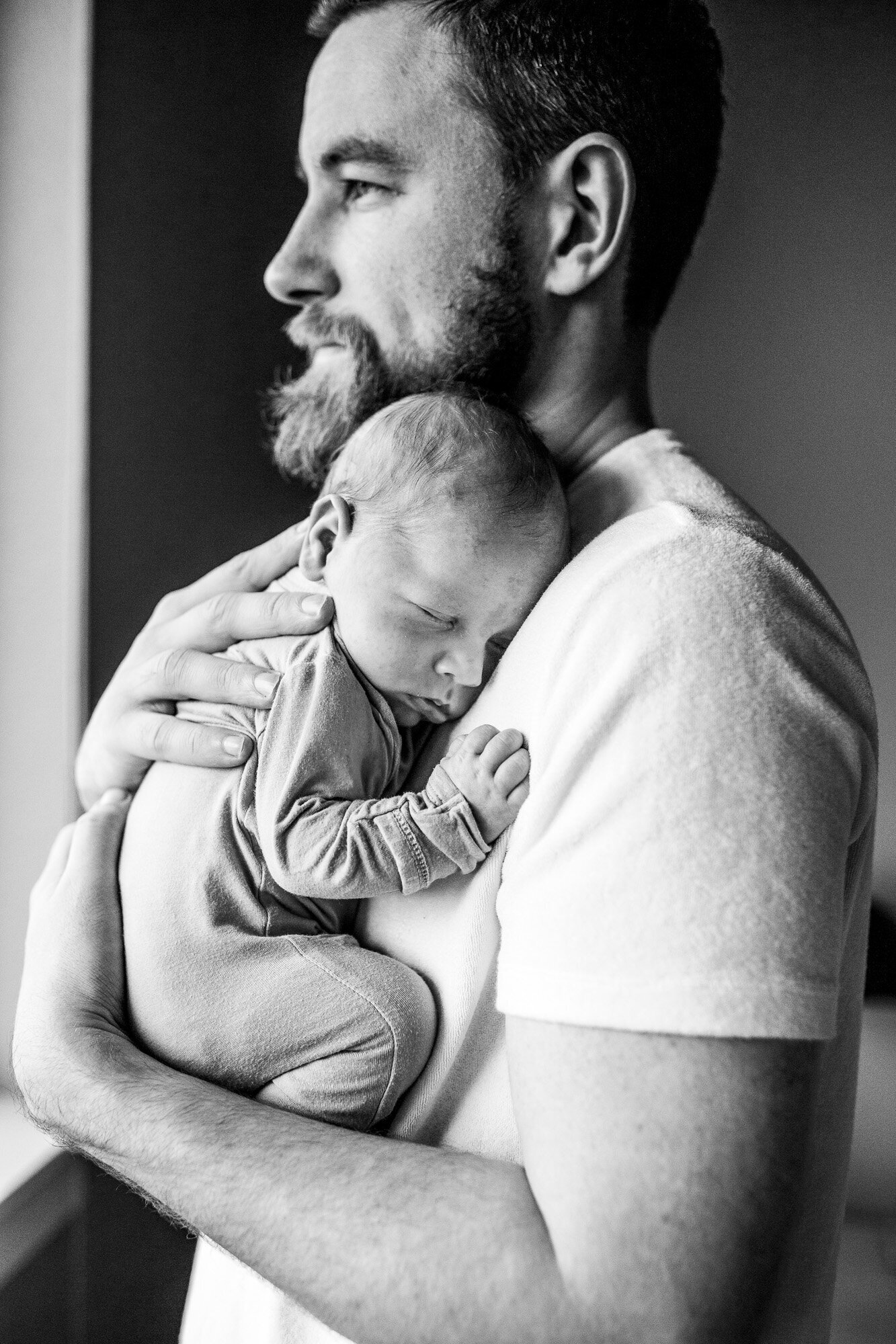 Black and white photo of dad holding newborn son by window. Portland newborn photography