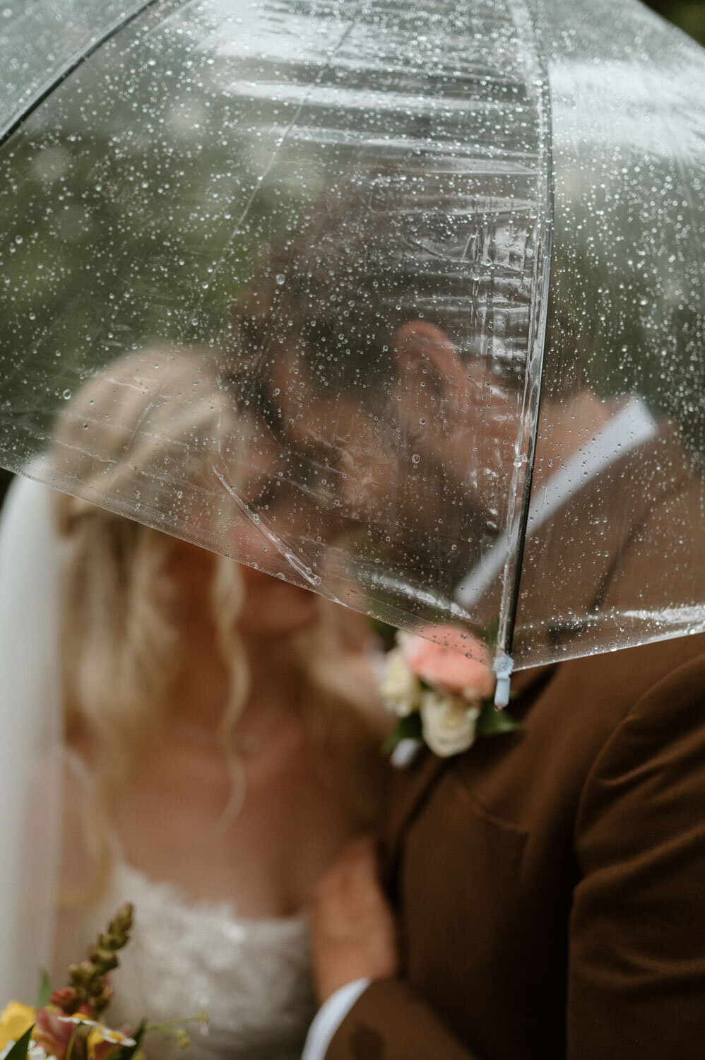 Bride and groom kissing under a clear umbrella