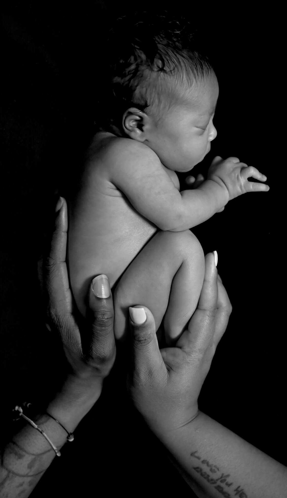 black and white photo of a mother with her hands cradling her newborn baby laying in the fetal position photographed by Millz Photography in Greenville, SC