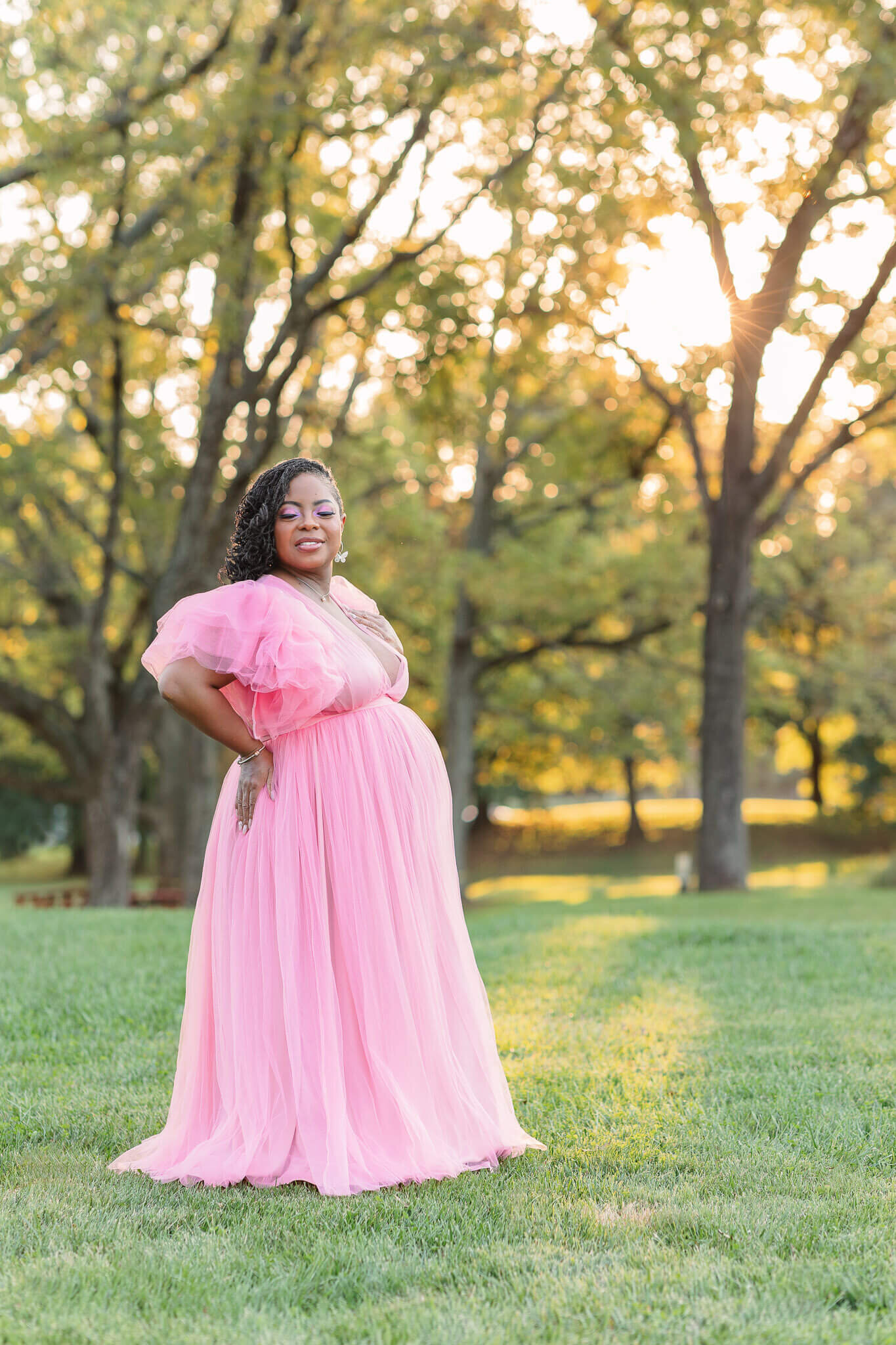 A pregnant woman in a pink dress posing in front of the sunset at a park in Northern VA.