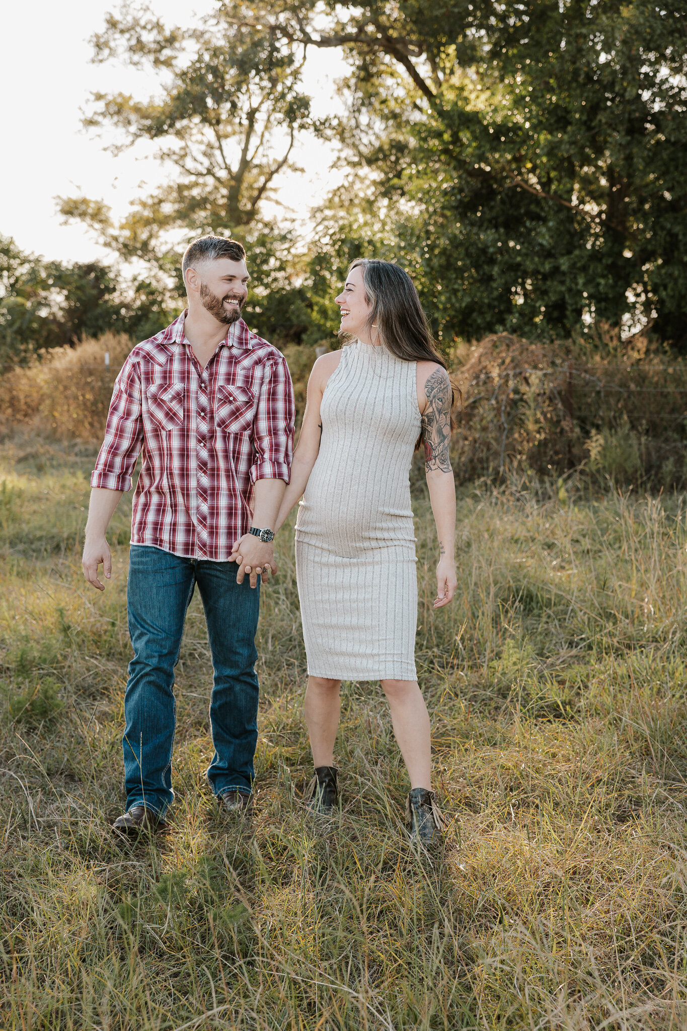 Outdoor maternity session in Aiken SC - expecting couple walking and holding hands in a golden field smiling and laughing at one another.