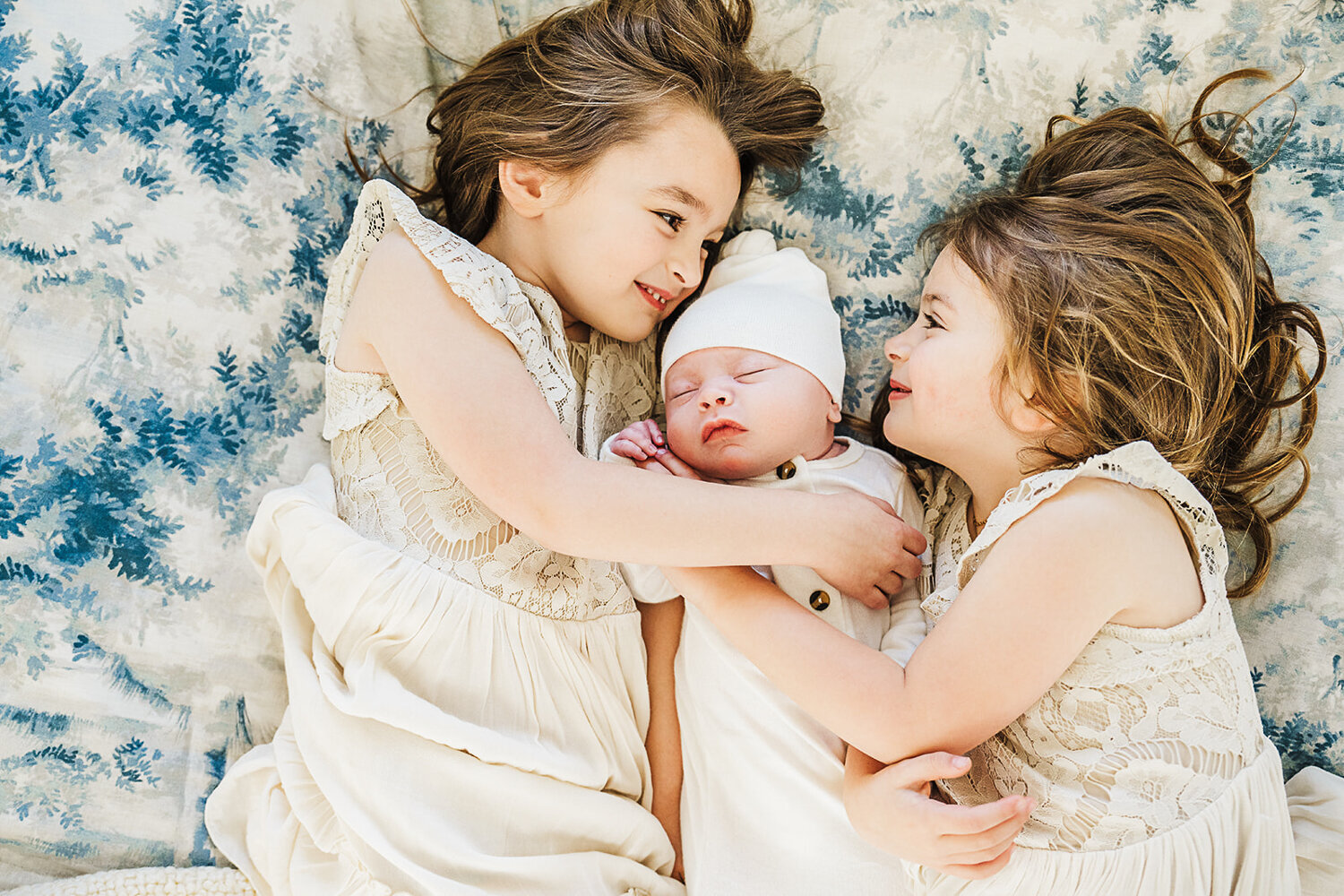 big sisters snuggle baby brother on bed boston newborn photography