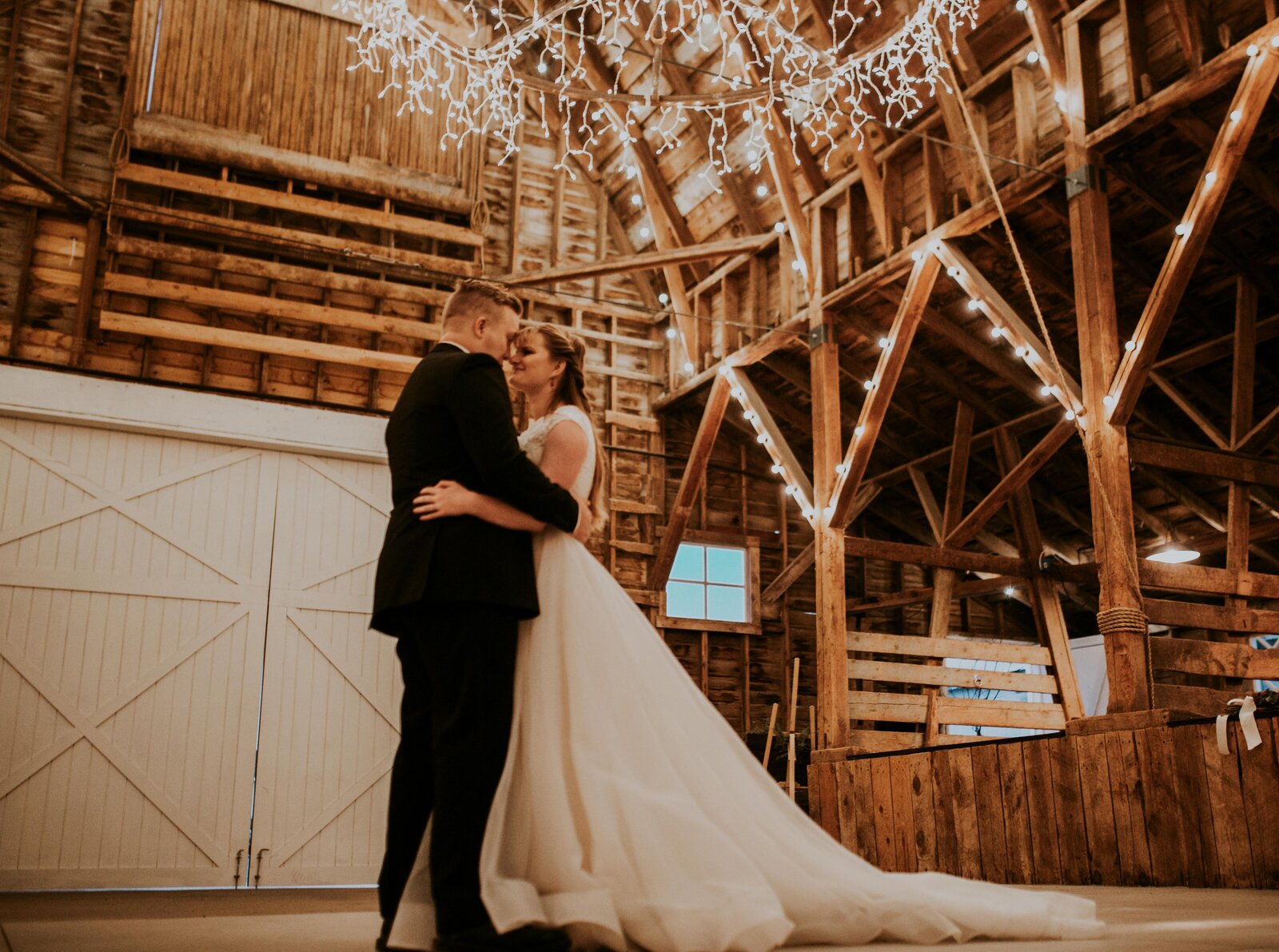 romantic barn with fairy lights and a bride and groom dancing alone together