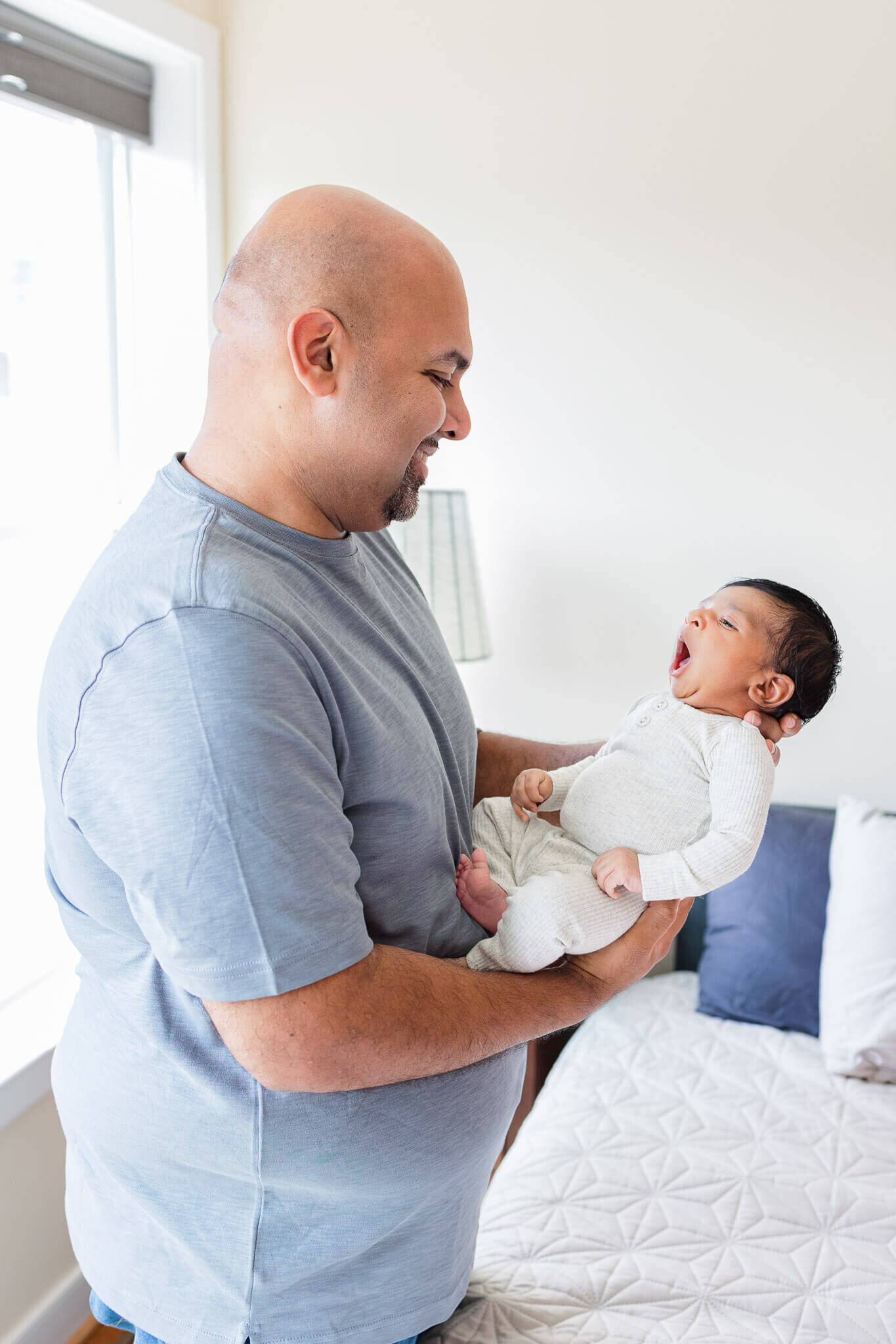 A dad holding his yawning newborn son.