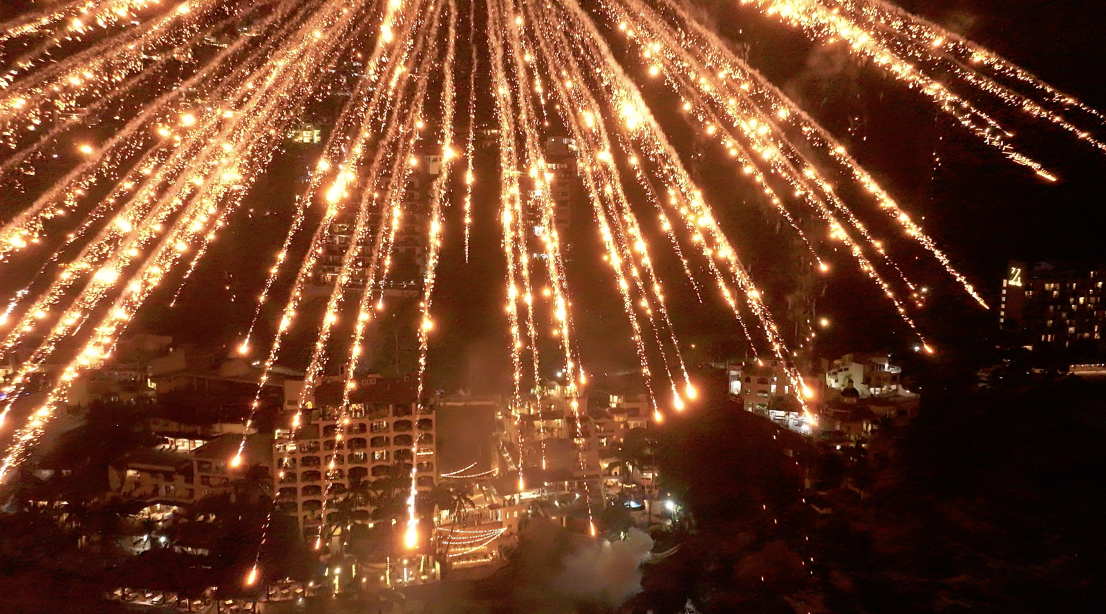 Aerial view of a nighttime fireworks display over a densely populated area, captured by a traveling wedding photographer.