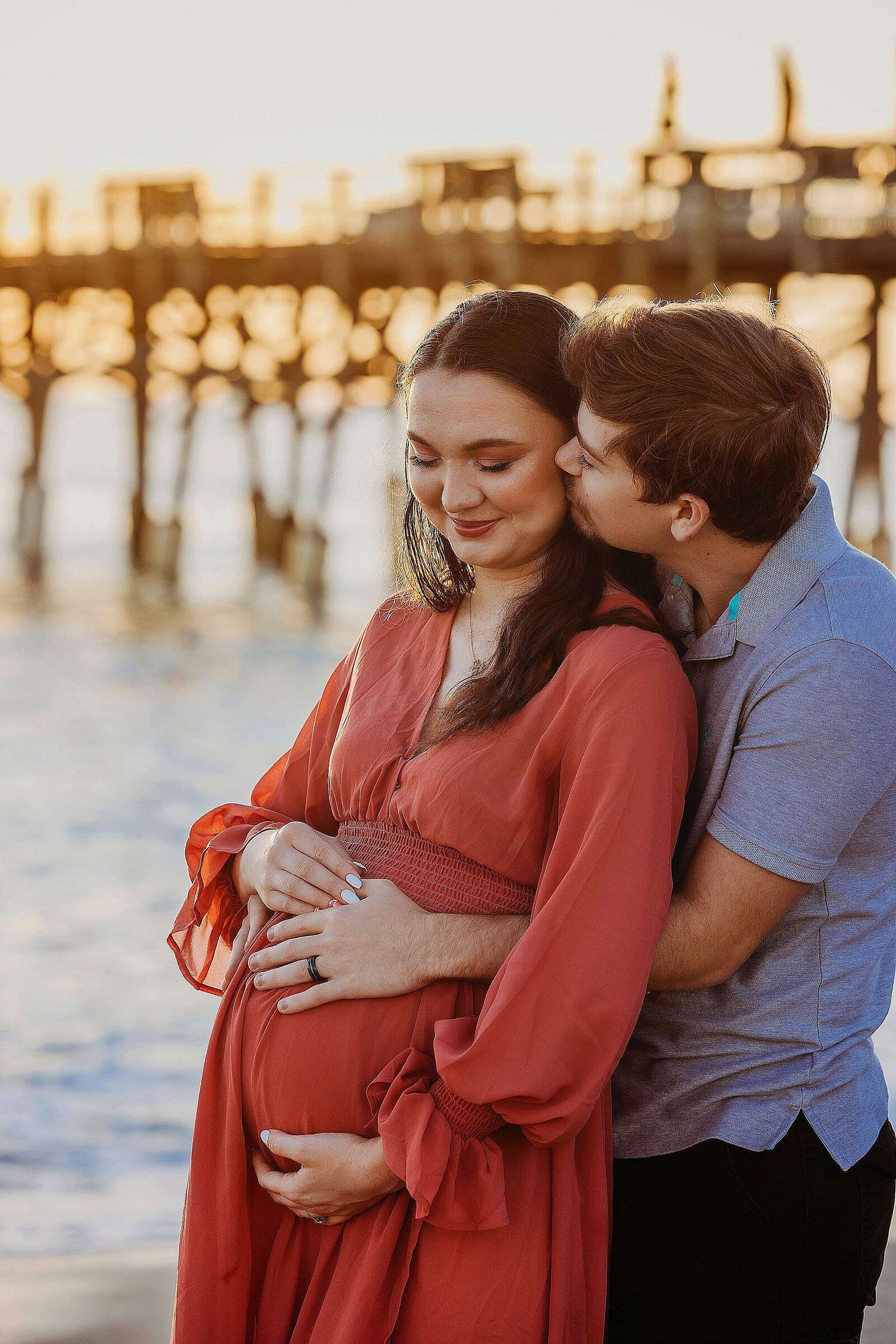 Pregnant couple enjoying a beach maternity session, captured by Bia Schaefer Photography, with waves in the background.