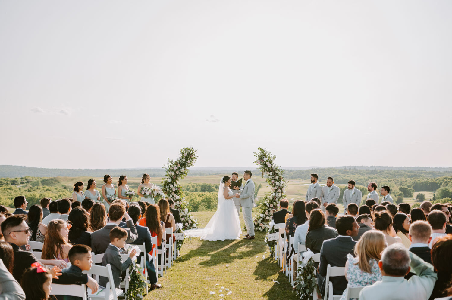Outdoor wedding ceremony with bride and groom under a floral arch
