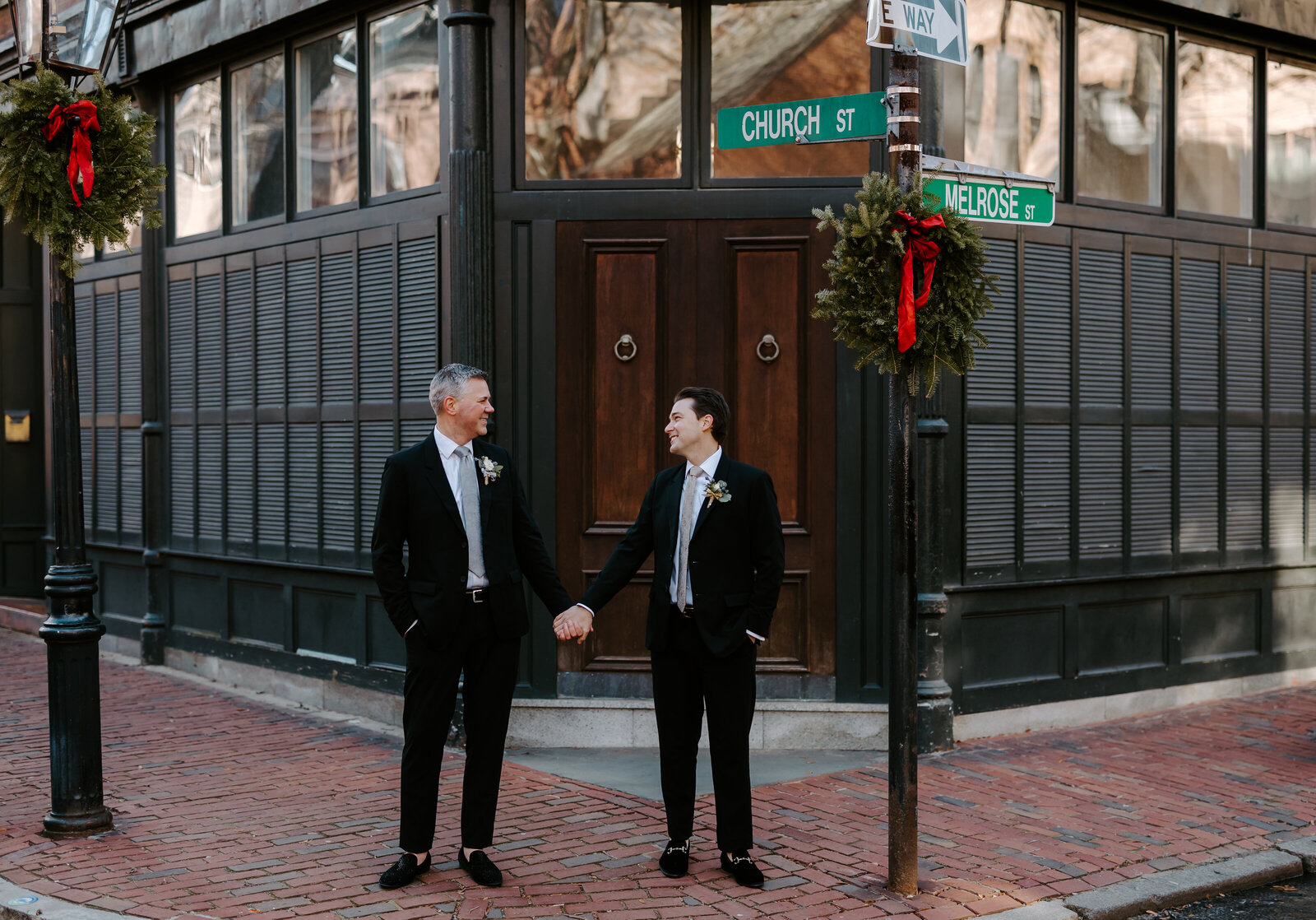Groom and groom hold hands and look at each other in front of their apartment building in Boston, Massachusetts