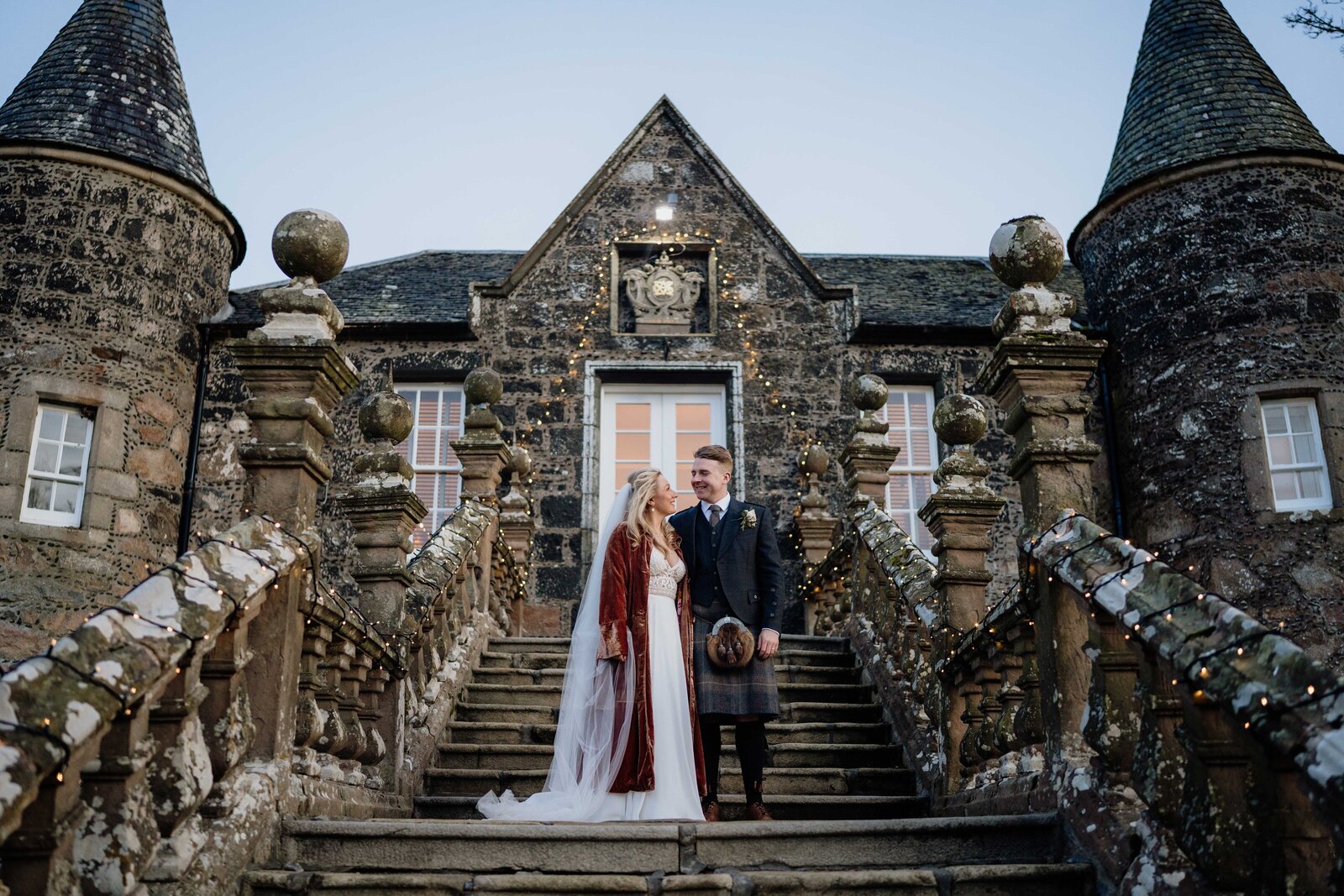A bride and groom stand on a grand outdoors staircase in the setting sun light. They are photographed after their wedding in Aberdeen.