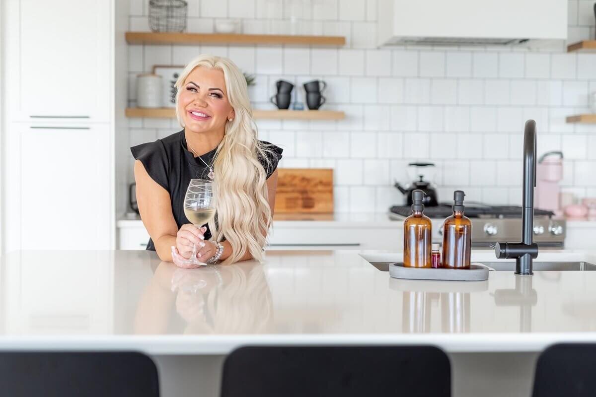 Lake country realtor in bright modern kitchen leaning on the island with a glass of wine