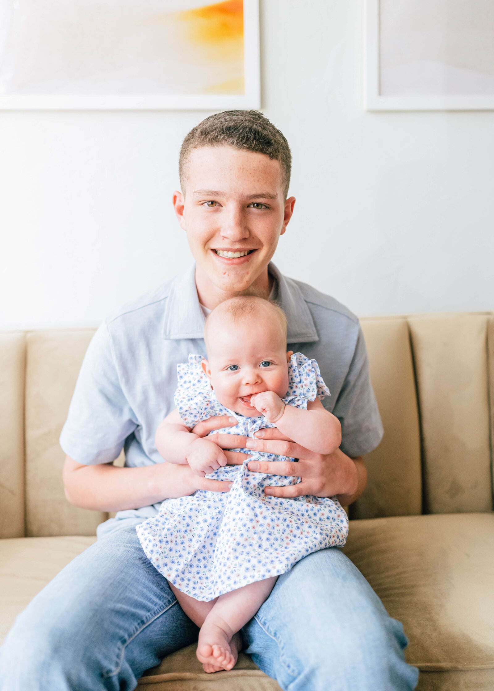 A teenage boy holds his infant sister while they both flash the camera a big smile