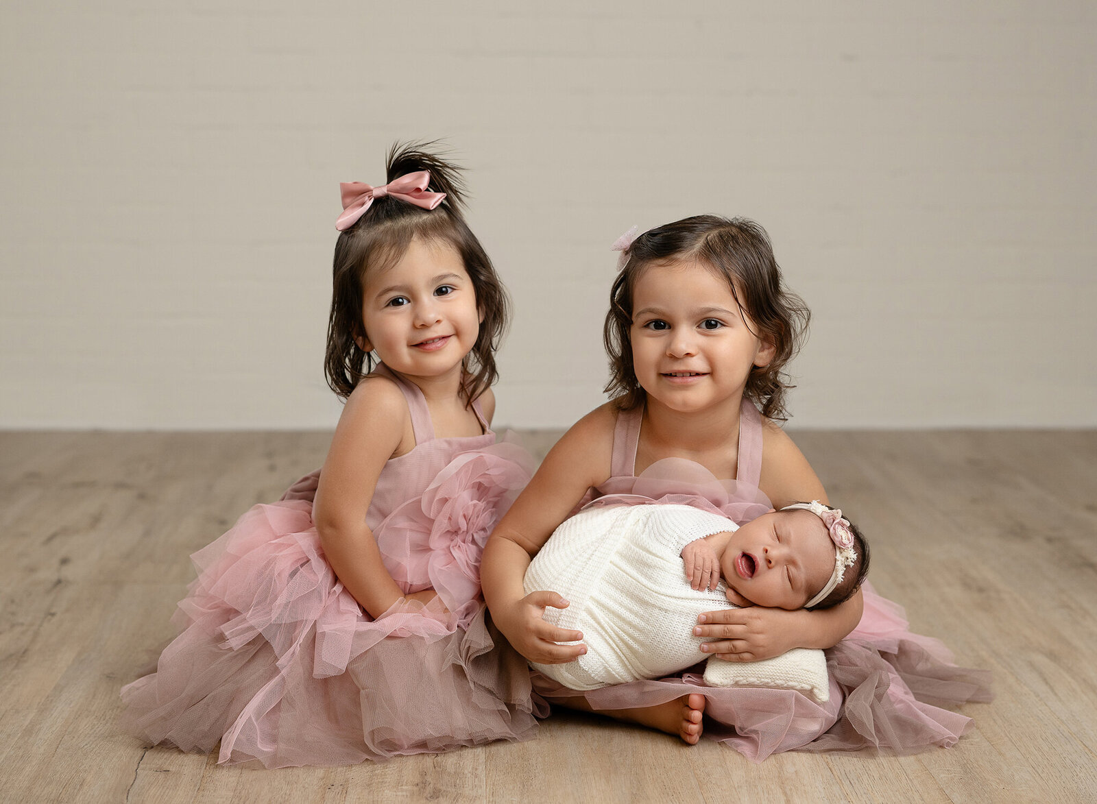Big sister holding baby and middle sister leaning in. Girl dressed in pretty pink tulle dresses and photographed at Atlanta photo studio.