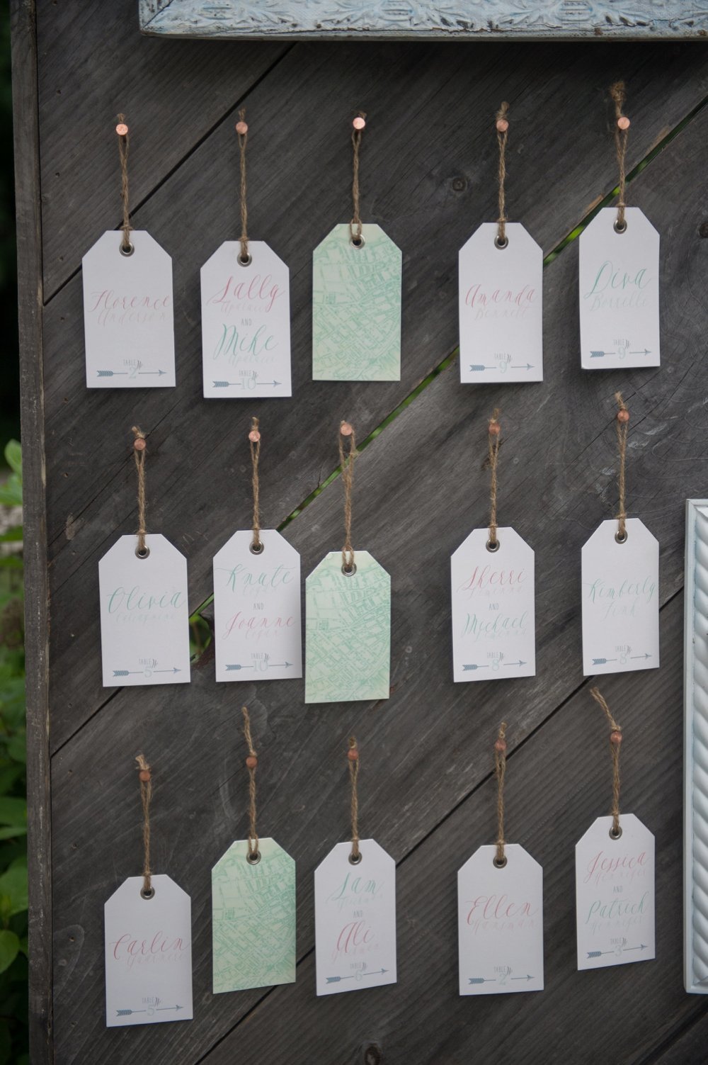 Wooden wall escort card display with tag escort cards and flowers in white frames at The Barn on Walnut Hill