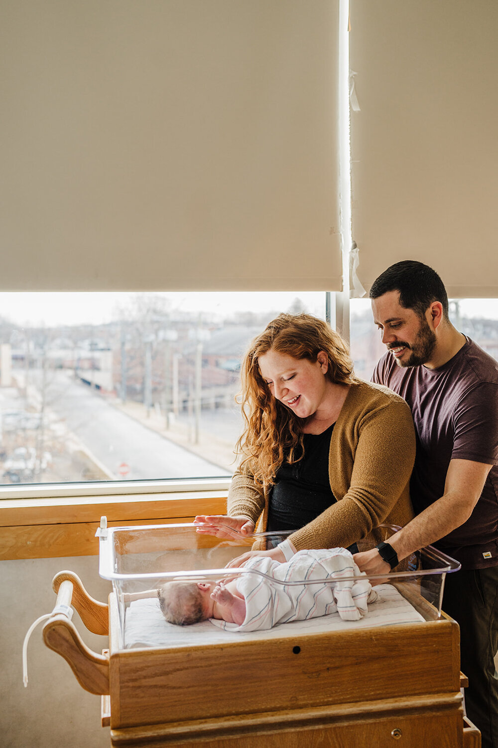 couple smiles down at baby boy in hospital bassinet