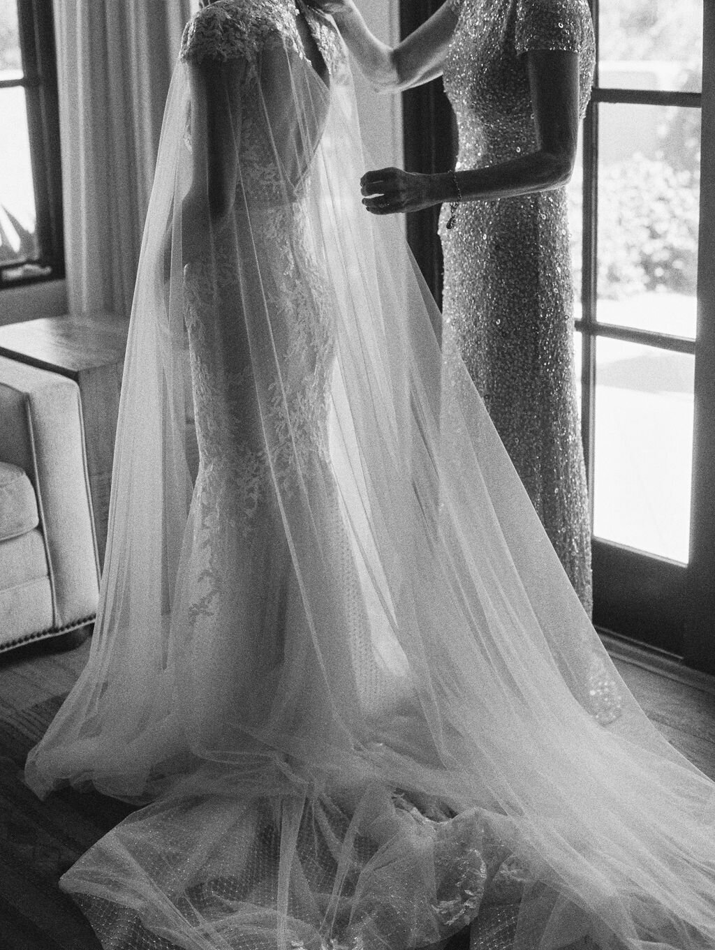 Black and white photo of bride getting ready  wearing lace gown by Berta with a tulle cape
