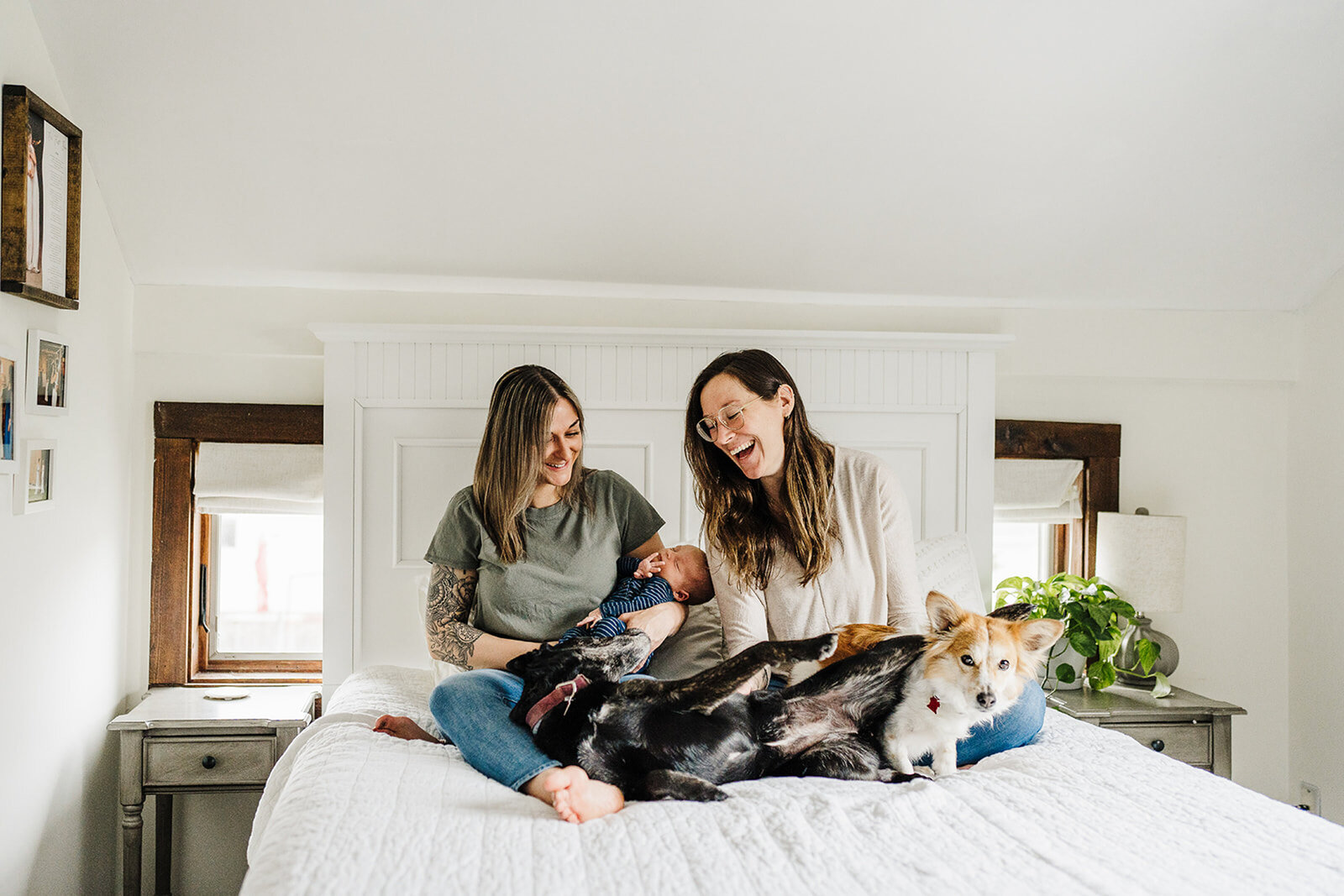 two moms laugh with dogs and baby in bedroom
