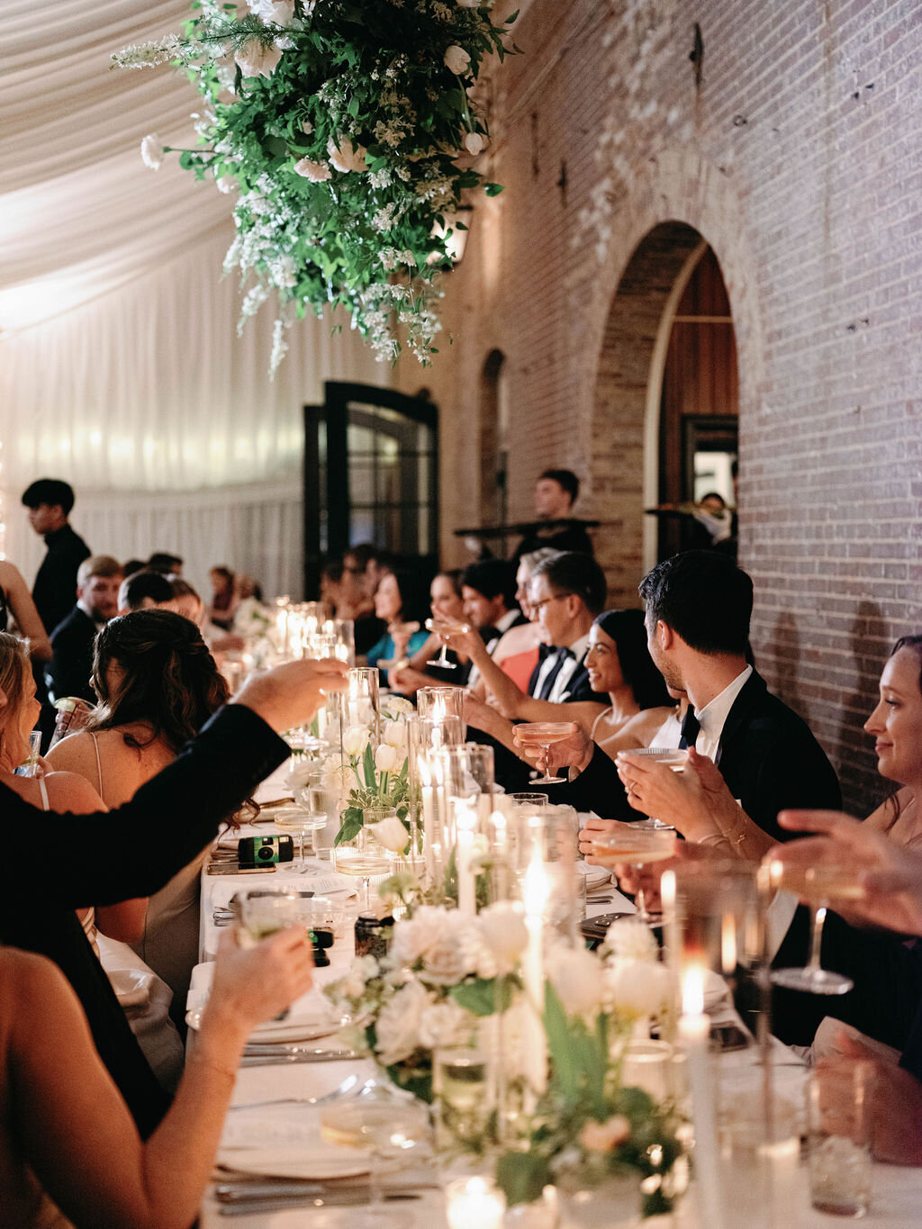 Guests sitting at a candlelit head table at reception Evergreen Museum Carriage House under a hanging installation