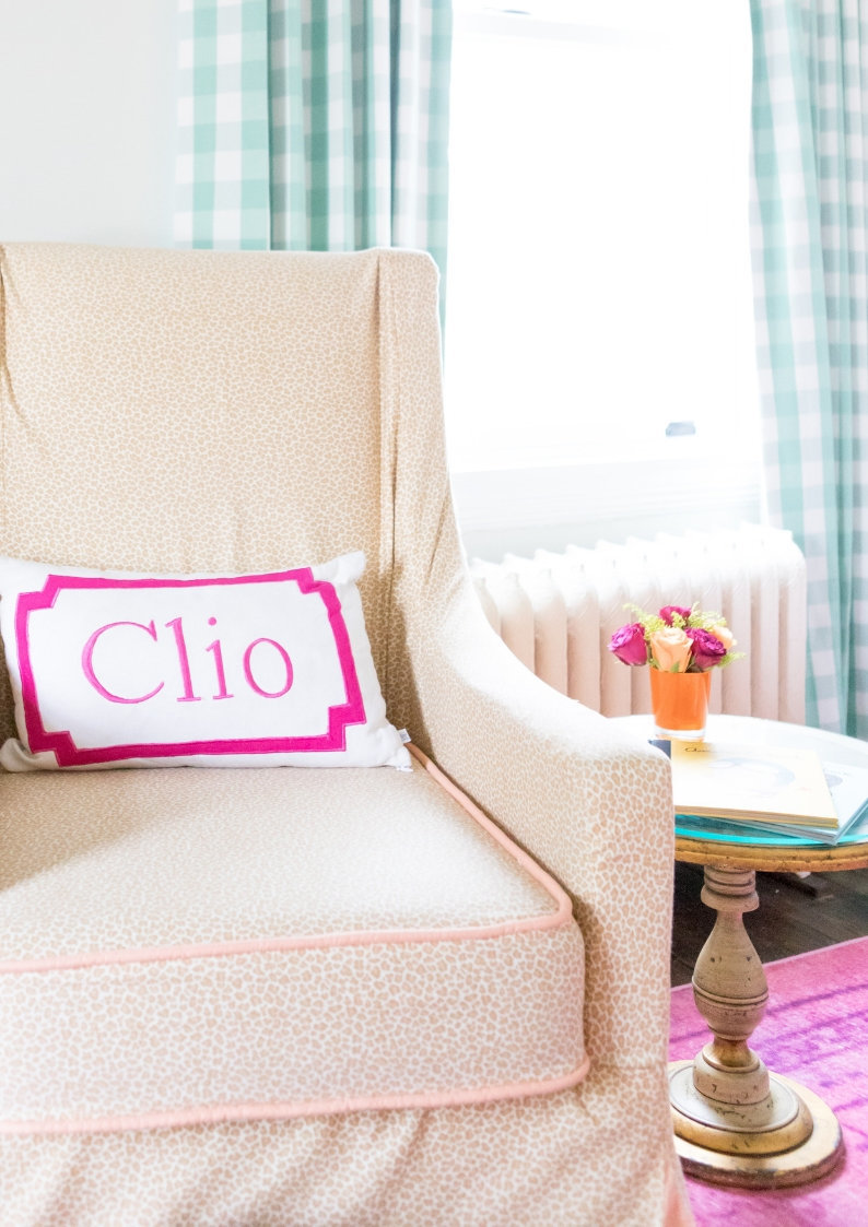 A light pink chair with a monogrammed pillow next to a small table.